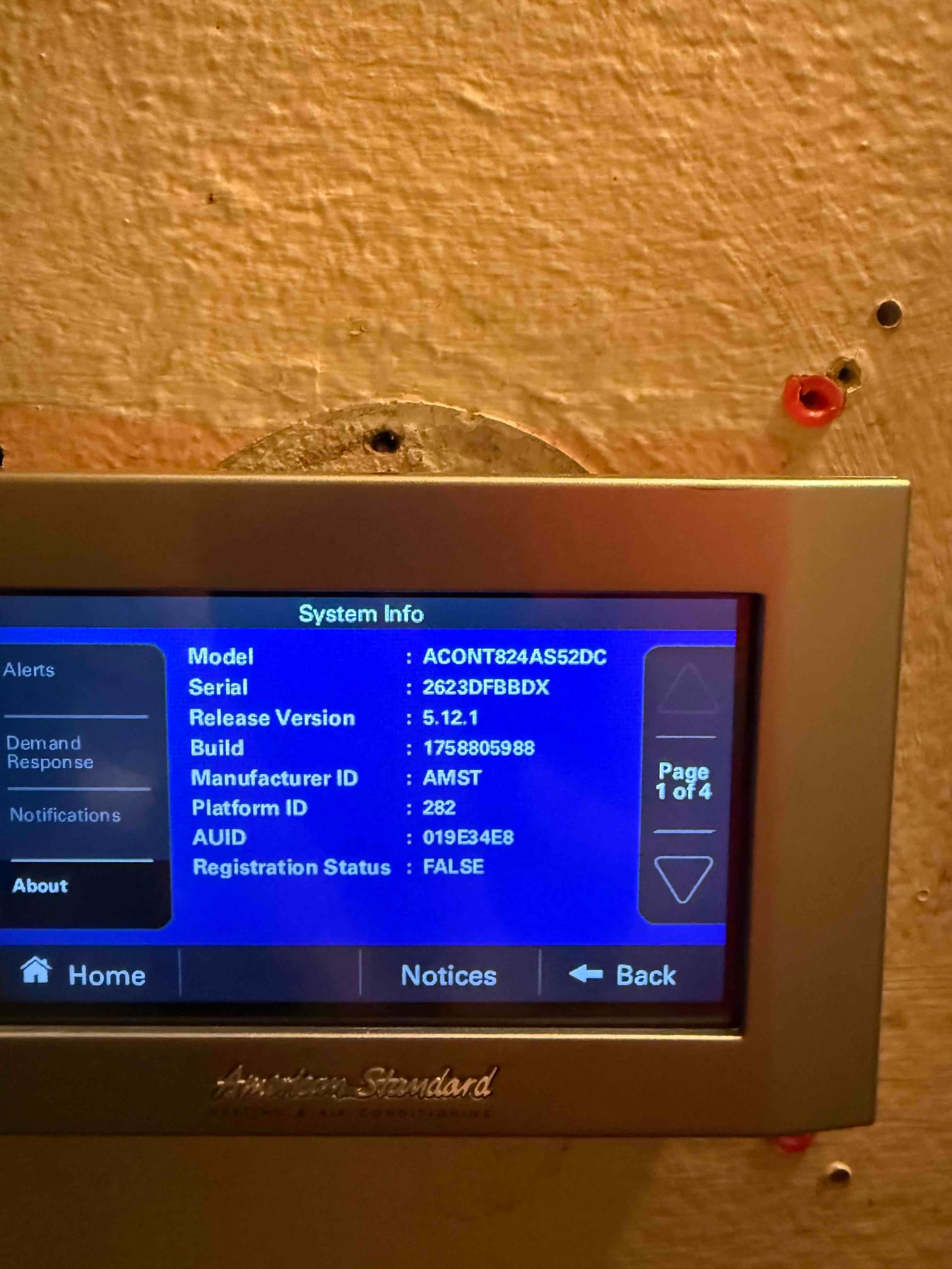 Wall-mounted touchscreen thermostat displays system information menu after installation, showing model, serial, and software details.
