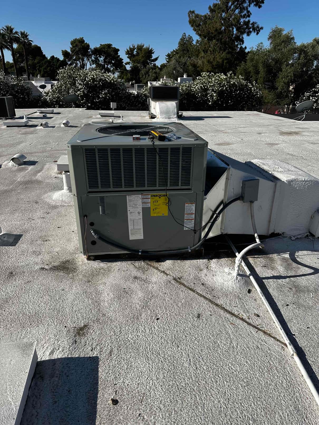 Packaged rooftop HVAC unit newly installed on a coated roof, connected to ductwork, electrical disconnect, and sealed penetrations.