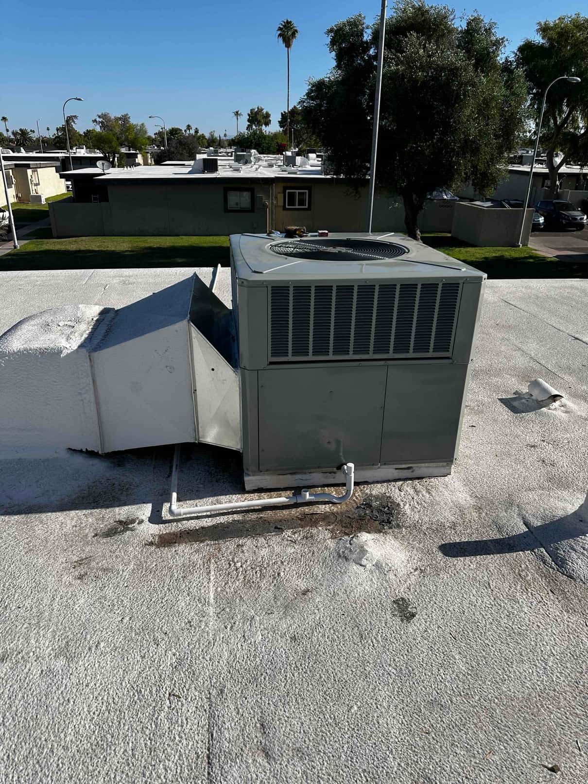 Rooftop packaged HVAC unit installed with connected ductwork and condensate drain piping, shown on a coated flat roof.