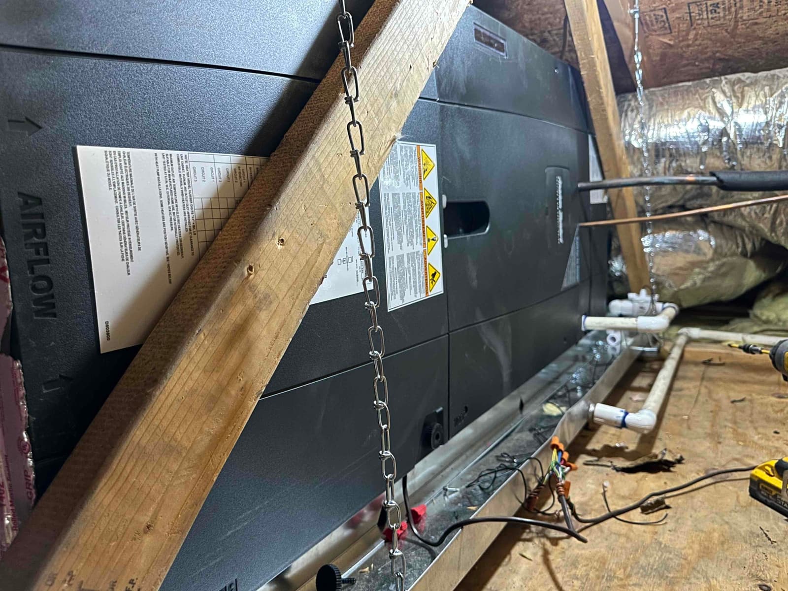 Air handler installed in attic with suspended support, insulated duct connection, and PVC condensate drain piping routed to the pan.