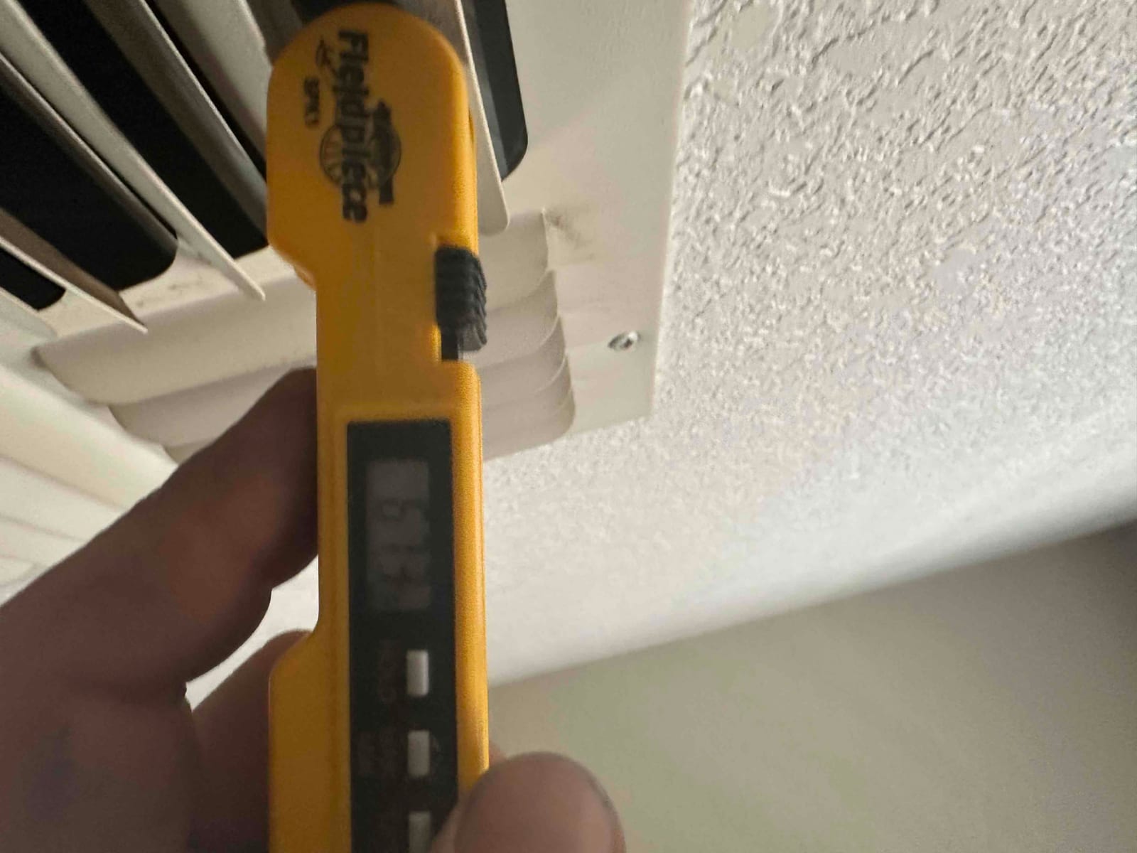 Digital thermometer at a ceiling supply register shows 63.9°F, documenting cooled air temperature from the new system.