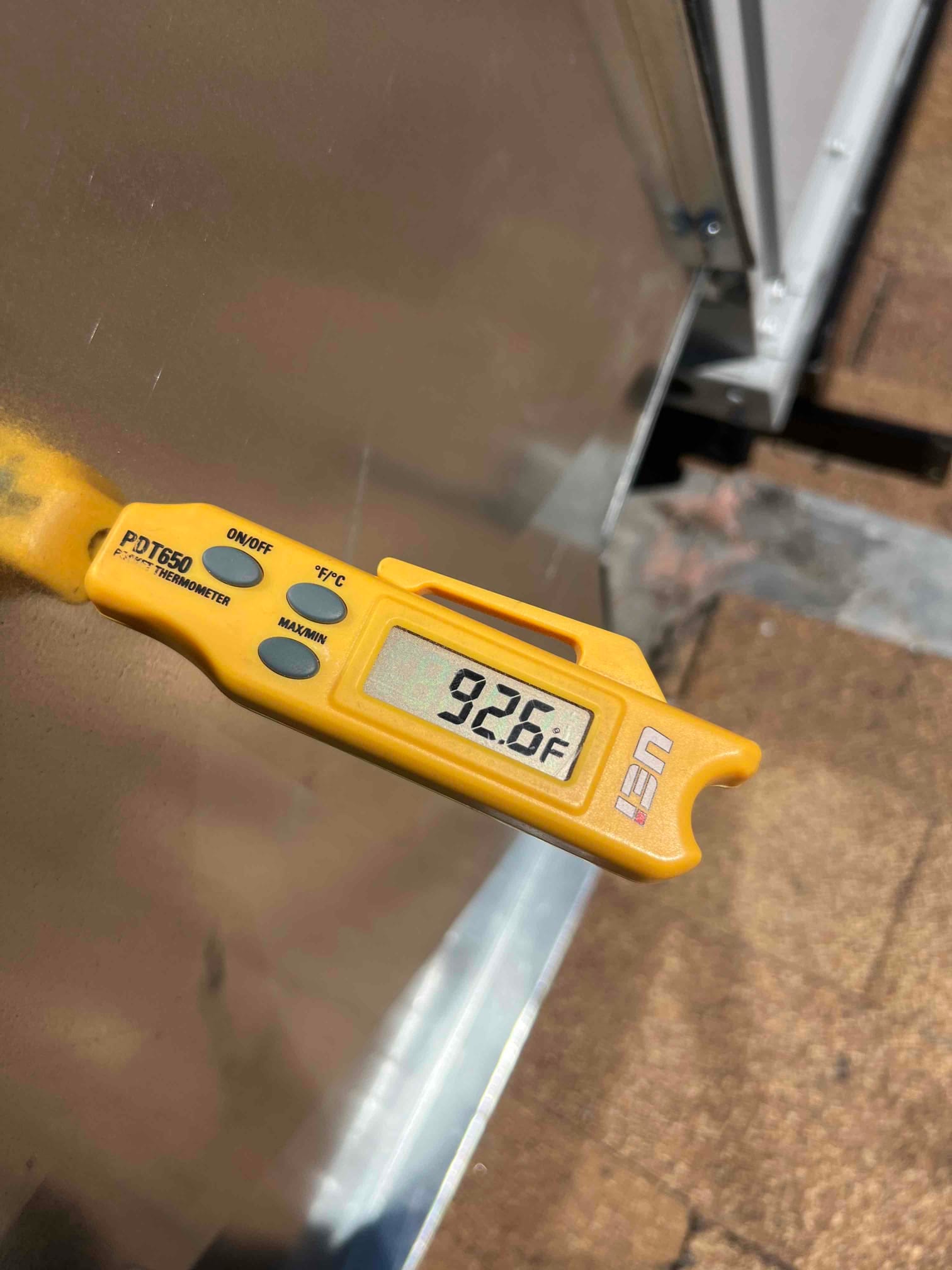 Digital thermometer displays 92.6°F while measuring air temperature during HVAC system commissioning.