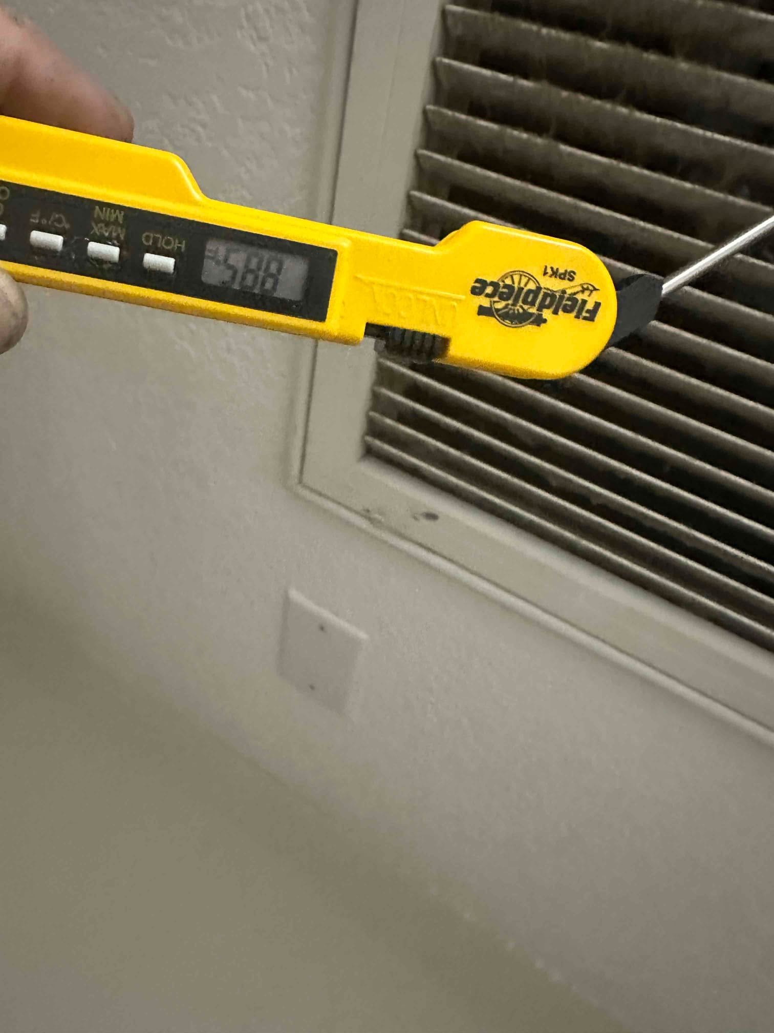 Digital thermometer probe measures air temperature at a supply register, with the display reading 58.8 degrees Fahrenheit.