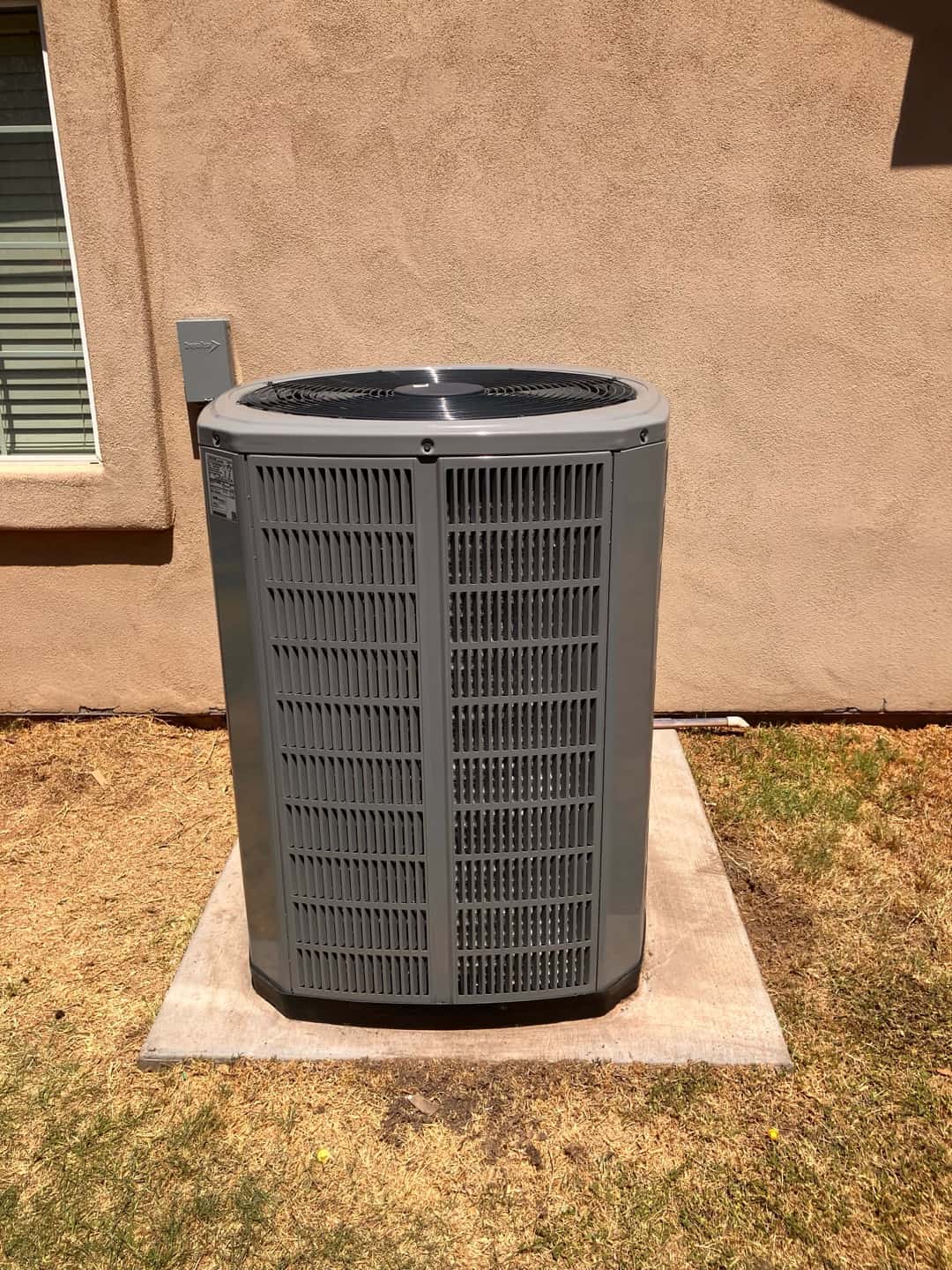 New outdoor heat pump condenser set on a level concrete pad with nearby electrical disconnect mounted on the wall.