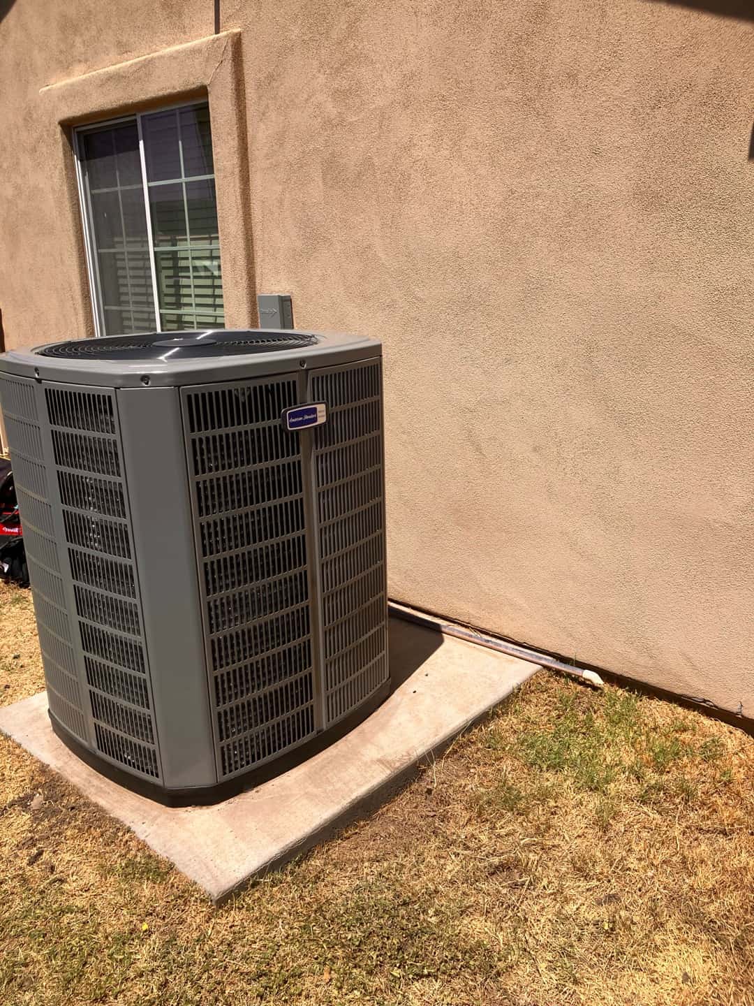 New outdoor heat pump condenser set on a level pad with insulated line set routed along the wall to the disconnect.