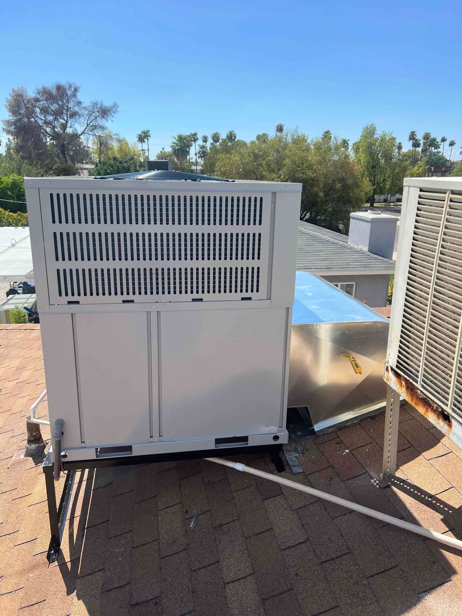 New packaged heat pump set on a rooftop stand with connected duct transition and condensate drain line routed across shingles.