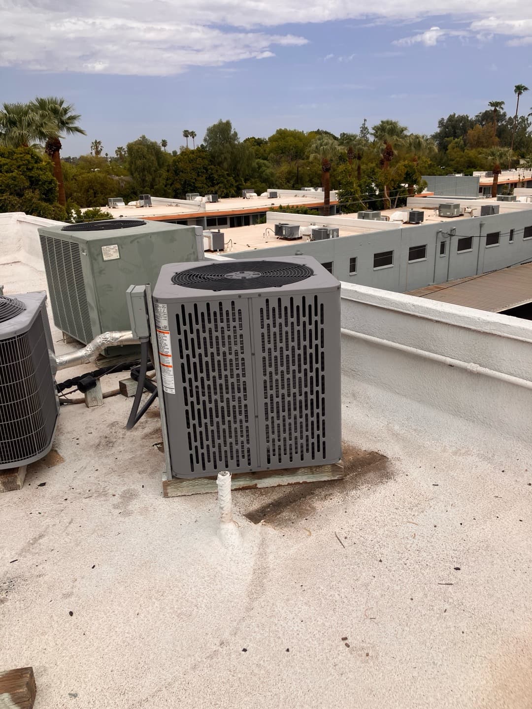 New rooftop condenser set on blocks with insulated line set and disconnect nearby, surrounded by other rooftop HVAC units.