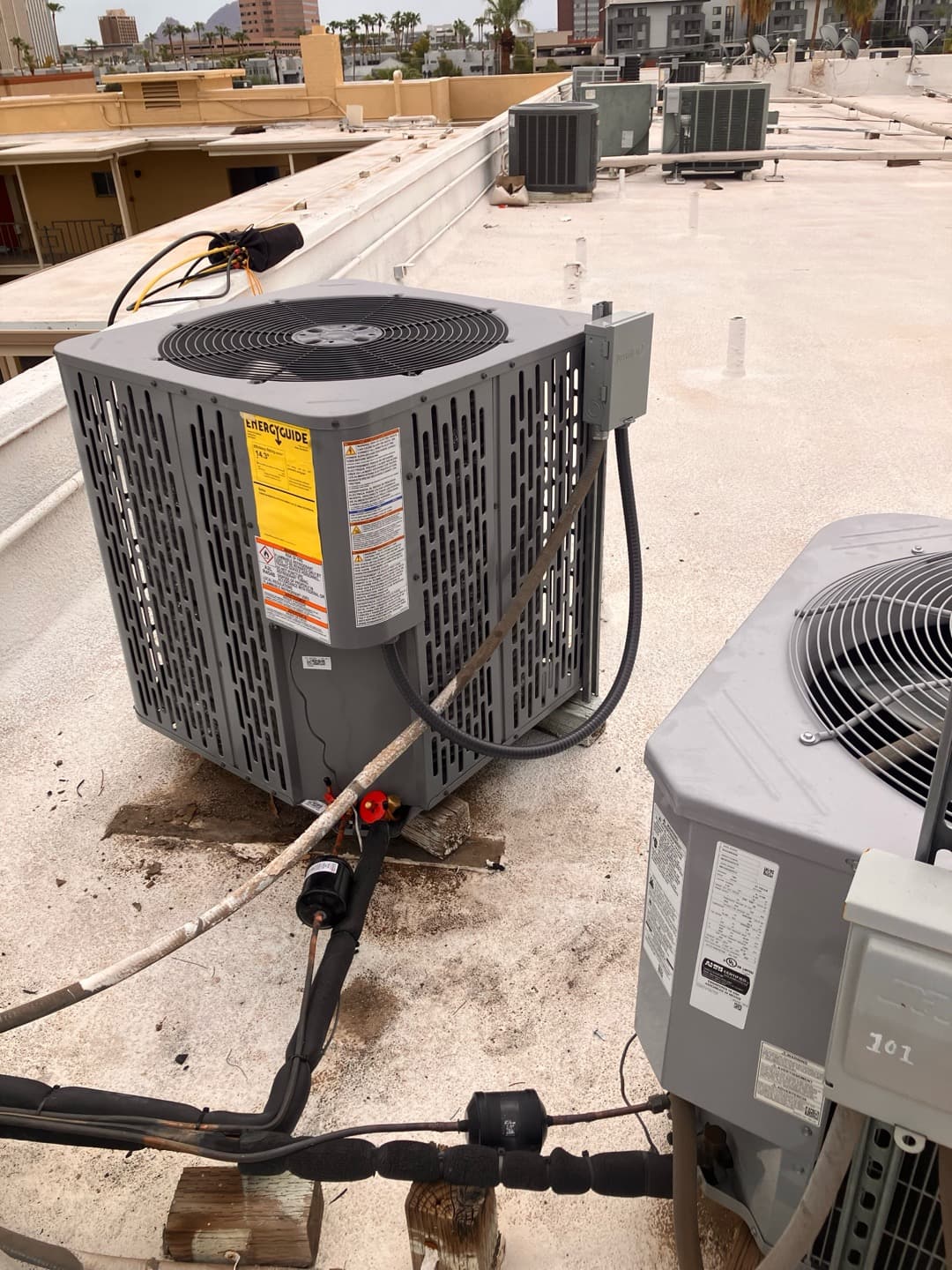 New rooftop condenser set on supports with insulated line set, filter-drier, and weatherproof disconnect installed alongside existing units.
