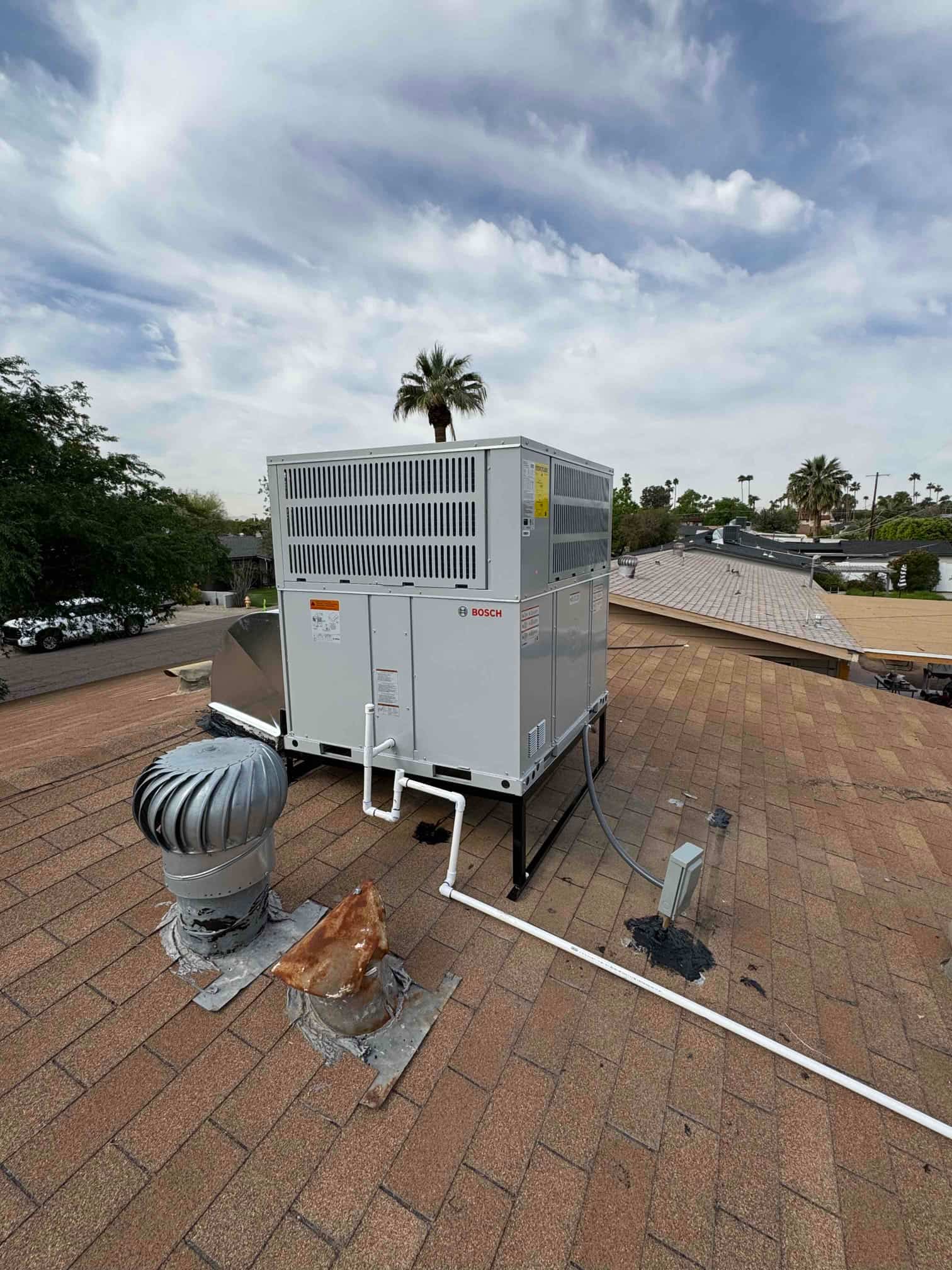 New rooftop package heat pump installed on a metal stand with condensate drain piping and electrical whip neatly routed.