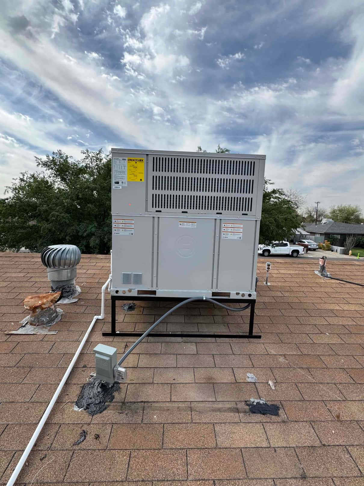 New rooftop package heat pump set on a metal stand with electrical disconnect and condensate drain piping routed across the shingles.