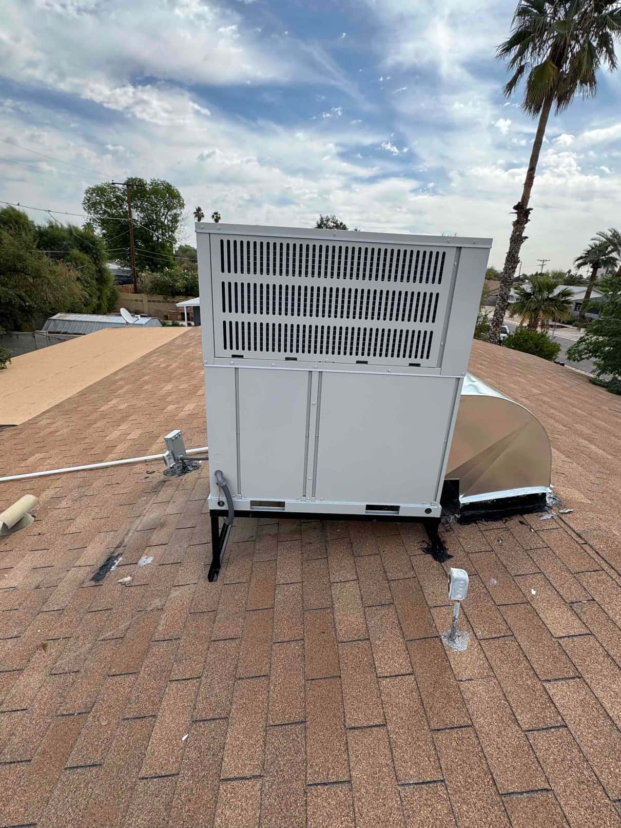 New rooftop packaged HVAC unit installed on stands with sealed curb and connected electrical whip visible on shingle roof.