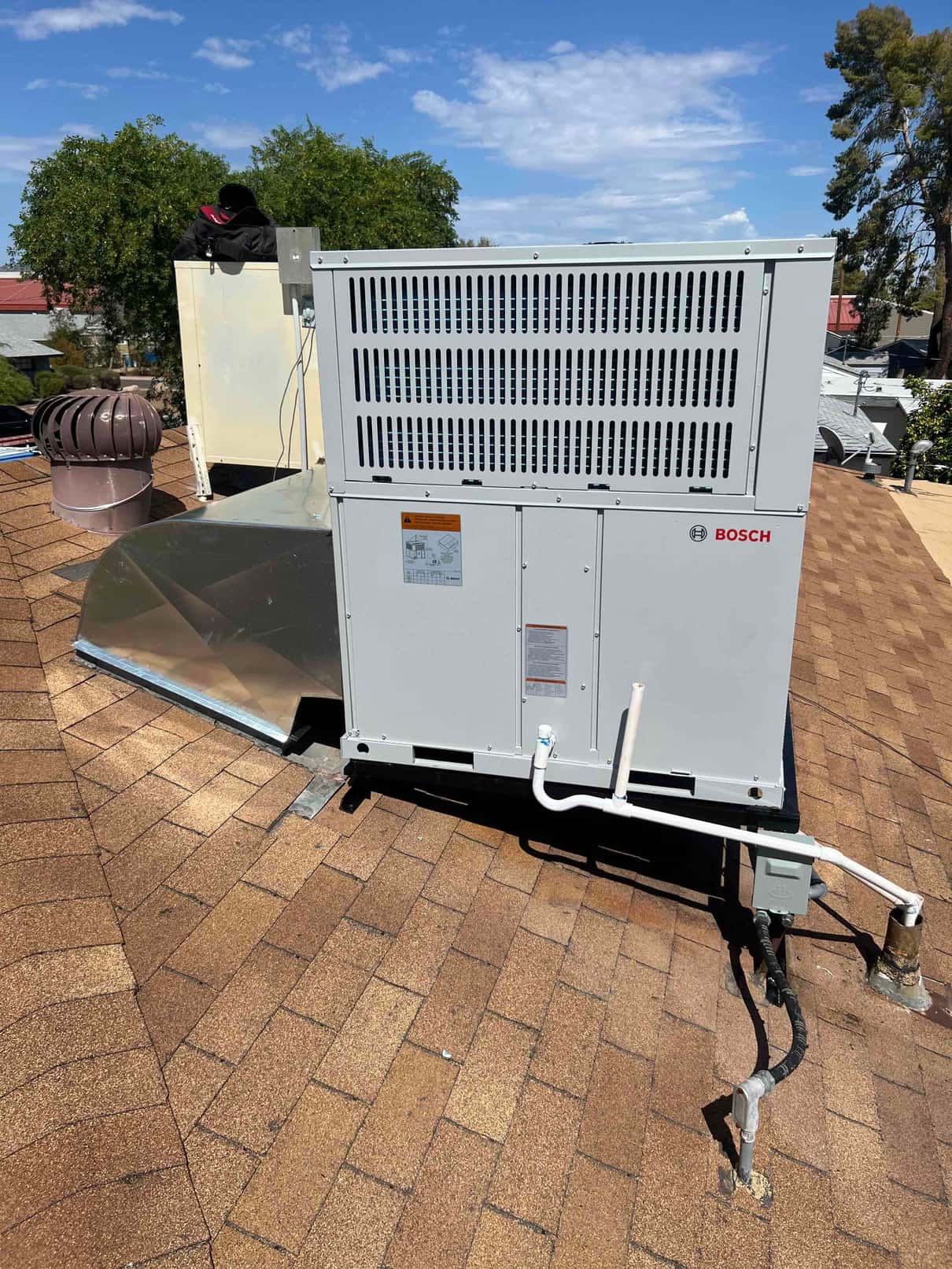 Rooftop packaged heat pump set on curb with new duct transition, condensate drain, and electrical disconnect installed.