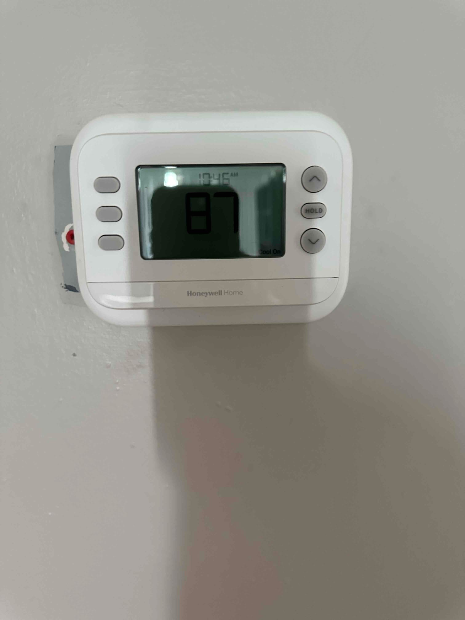 Wall-mounted digital thermostat installed and powered, display showing room temperature and control buttons.