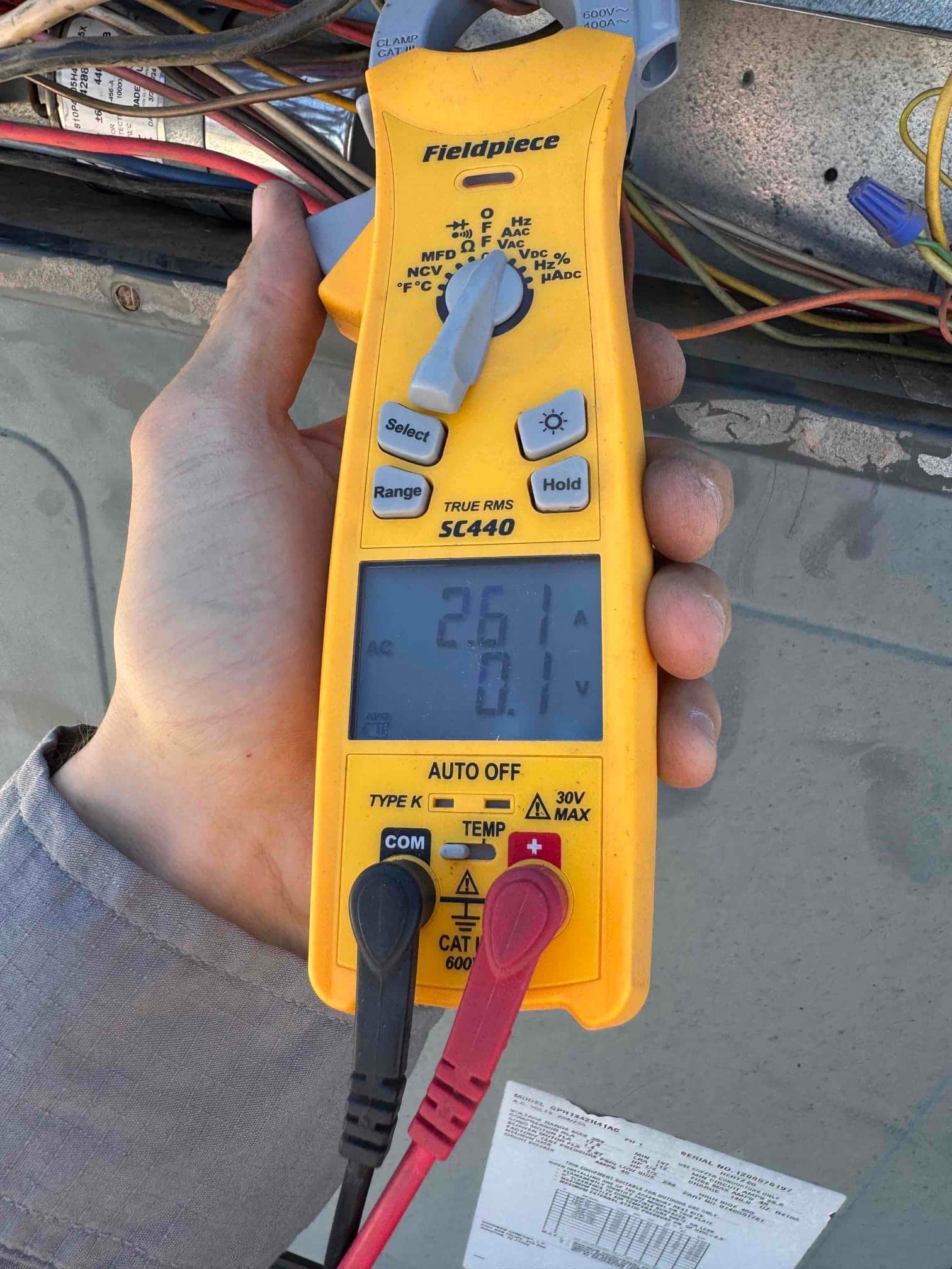 Clamp meter measures AC voltage at the test leads, displaying 26.1 V on the screen during the diagnostic check.