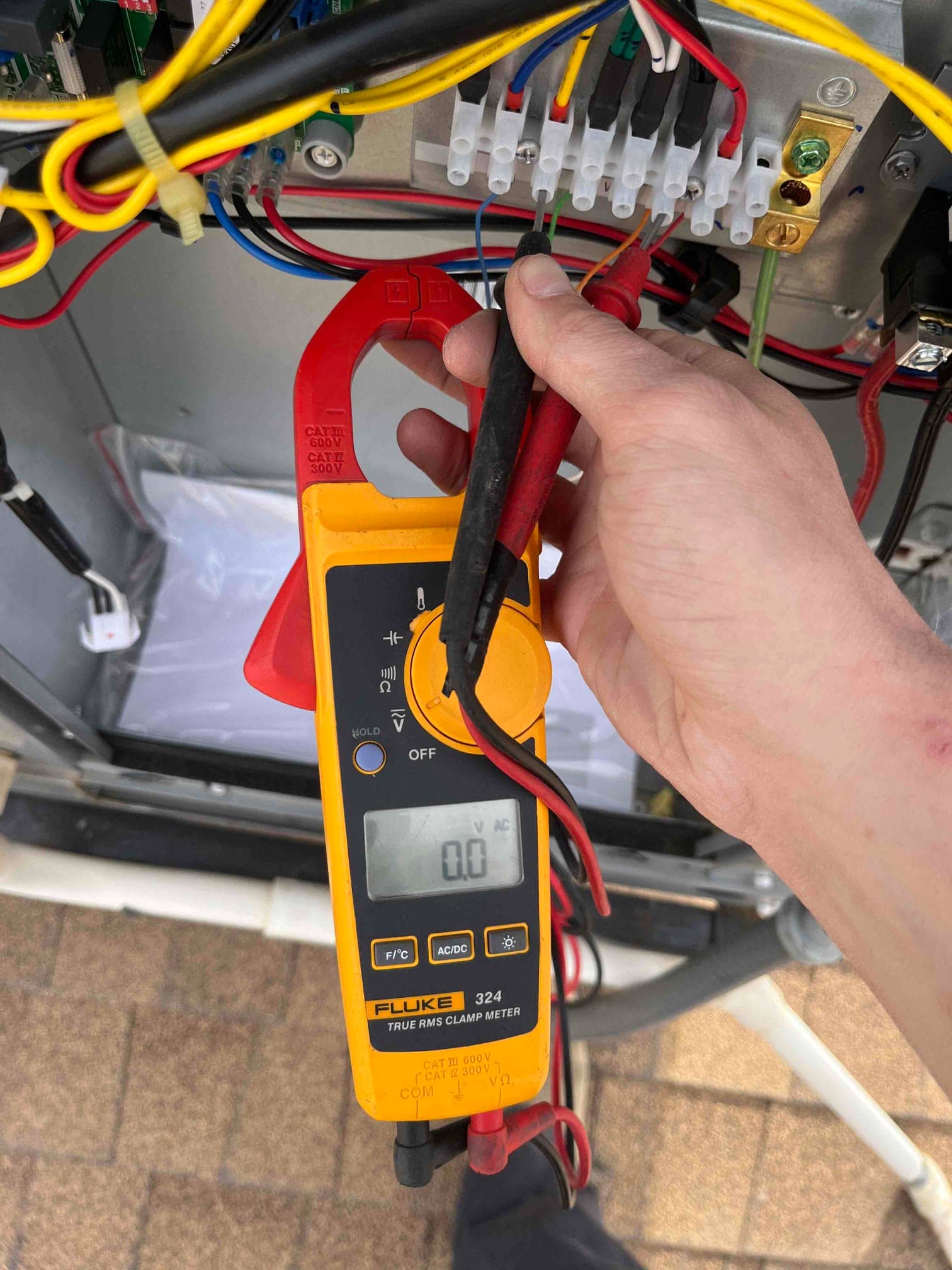 Clamp meter shows 0.0 V AC while probing a control terminal strip inside the HVAC unit.