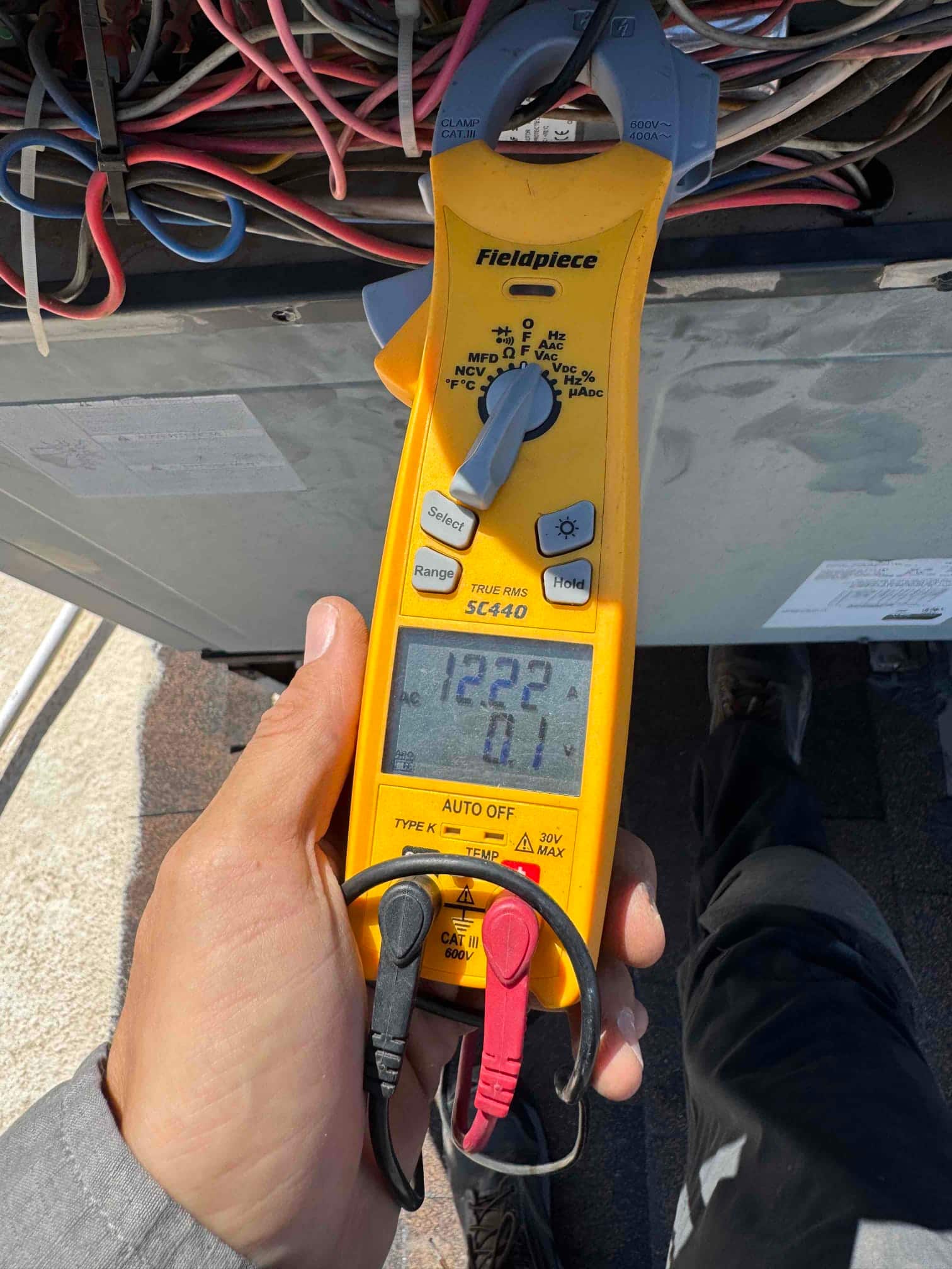 Clamp meter shows 12.21 A on a conductor while measuring current during air conditioner service.