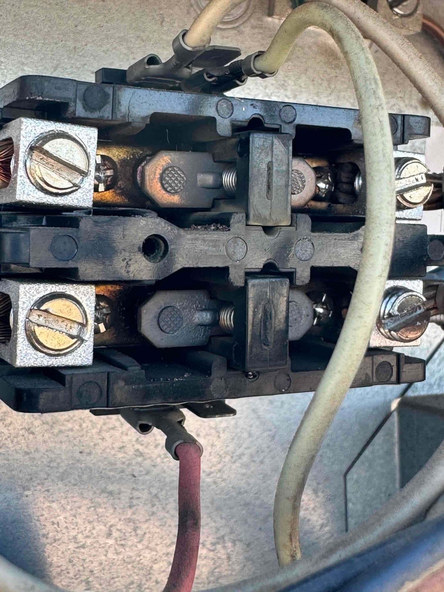 Close-up of a 2-pole contactor with connected wires, showing heat discoloration and worn contact surfaces inside the condenser unit.