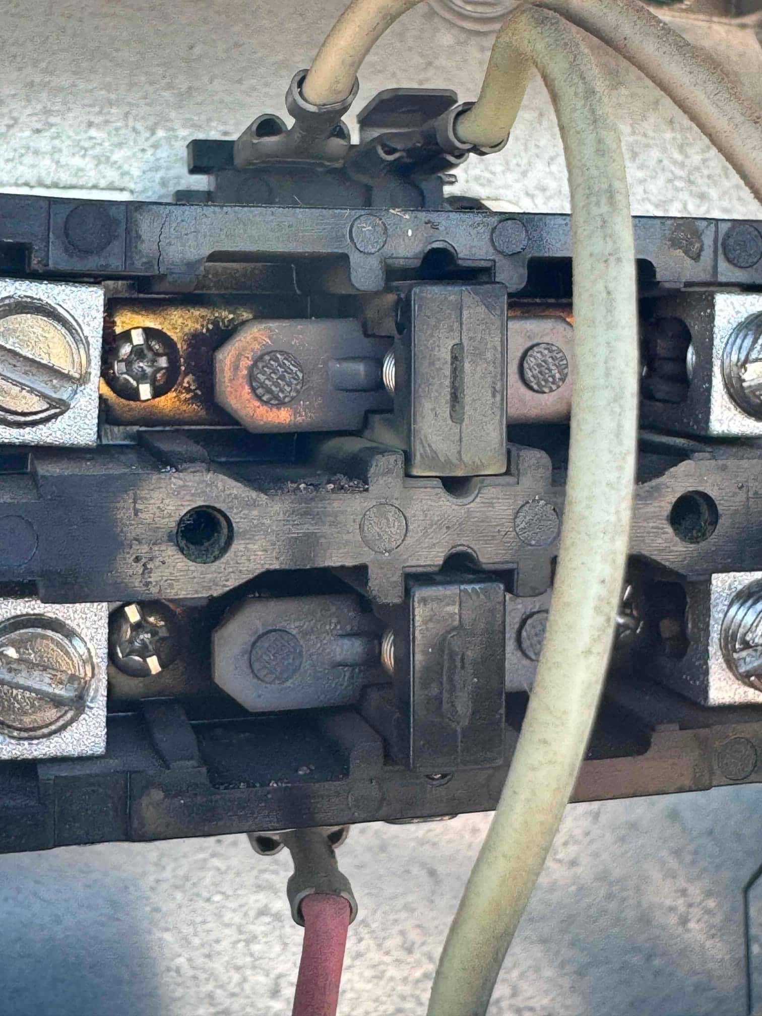 Close-up of a two-pole contactor showing heat discoloration and pitted contacts with connected wiring and terminal screws.