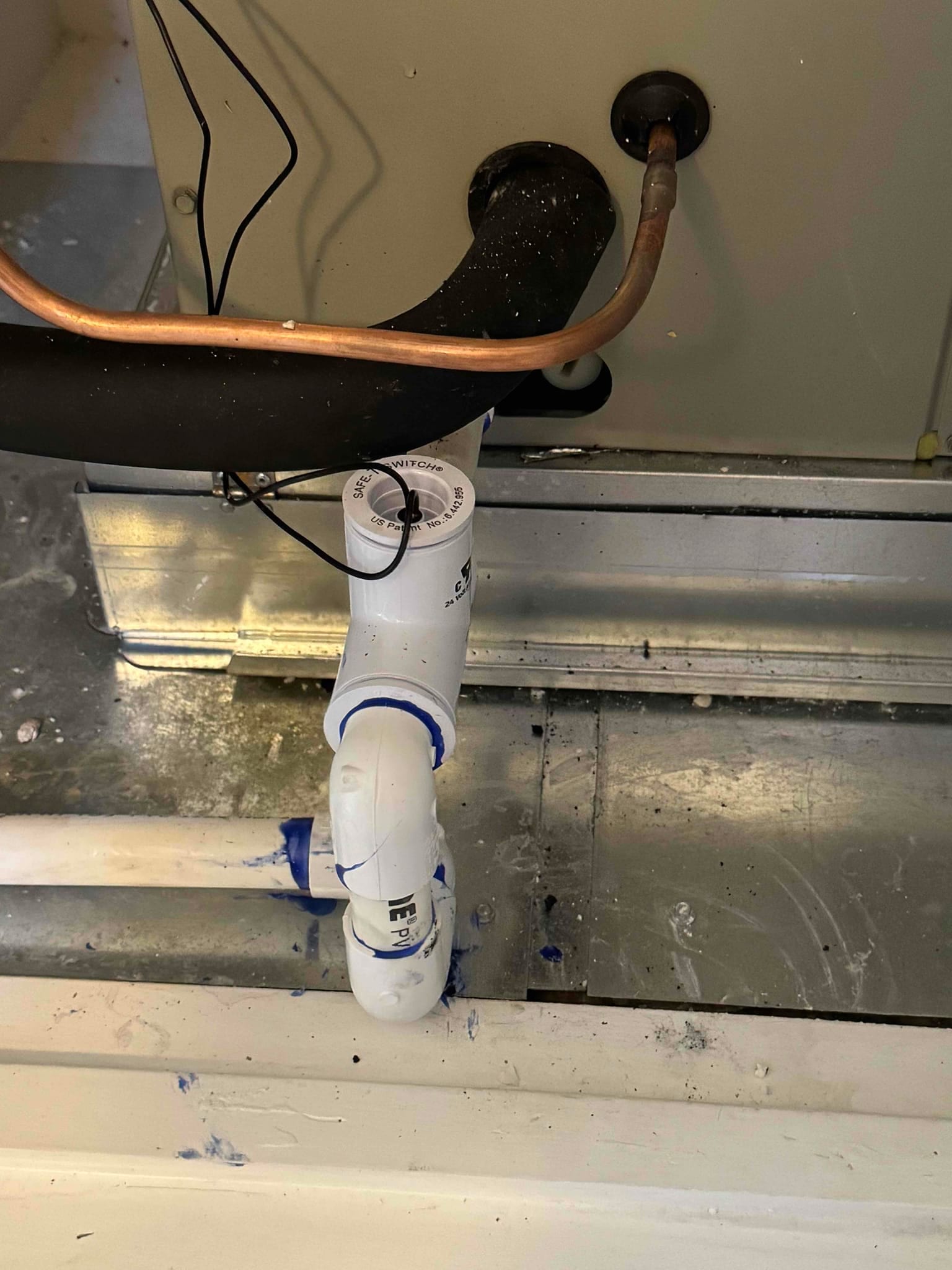 Condensate drain assembly with float safety switch installed at the air handler, glued PVC fittings, and insulated refrigerant line nearby.