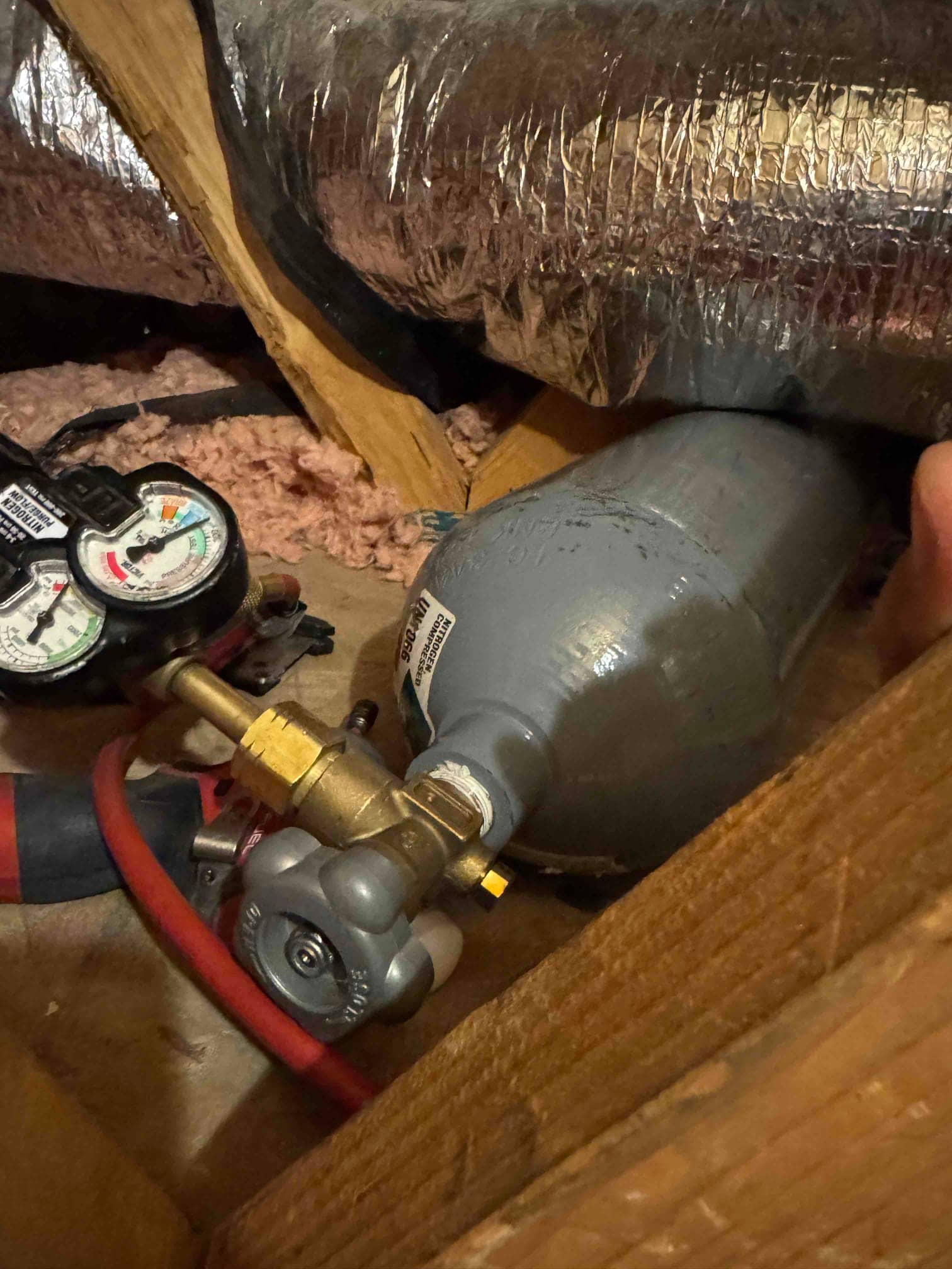 Condensate drain line trap assembly with vent cap and attached hose in attic near insulated ductwork.