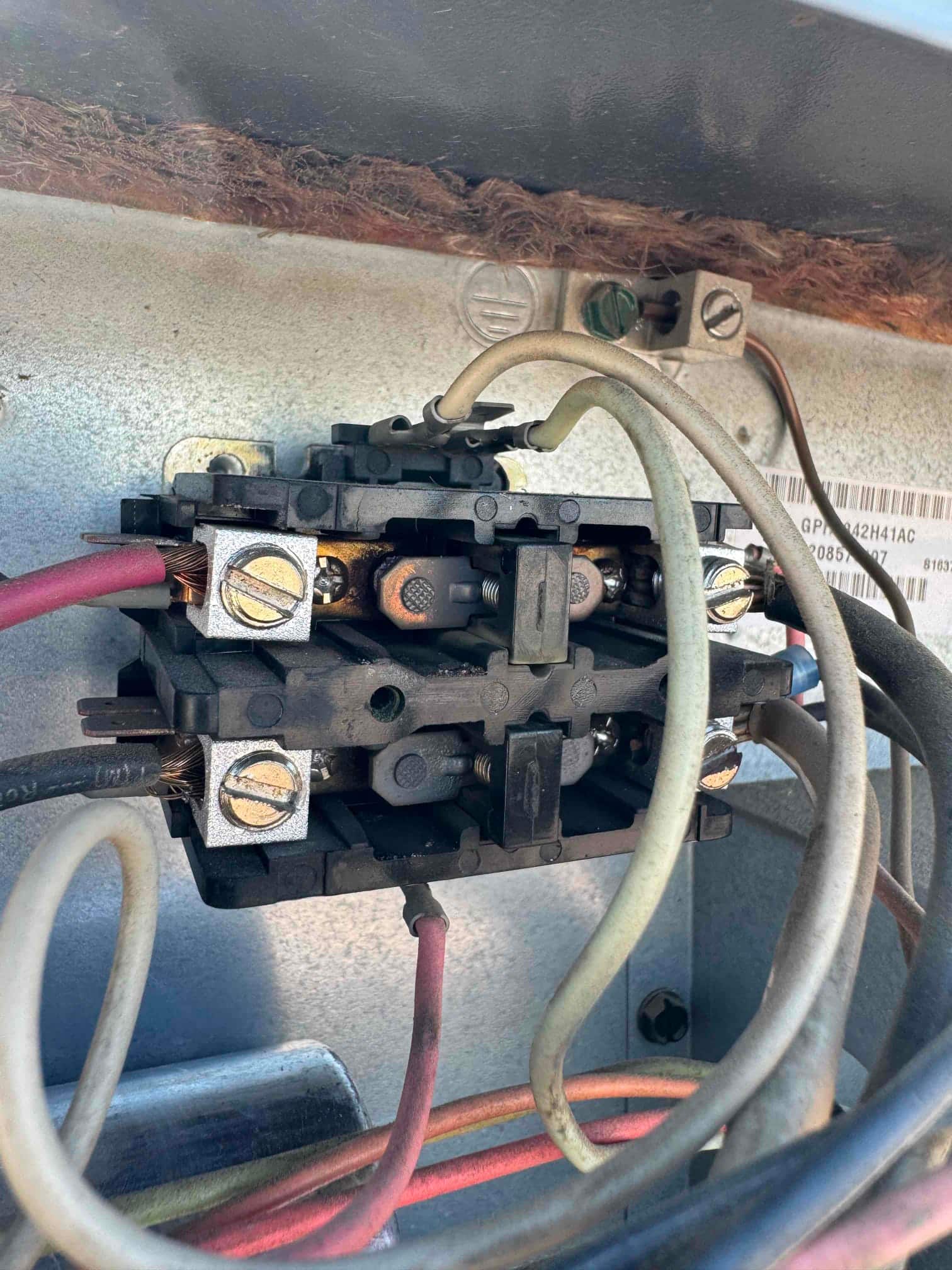 Contactor with multiple connected wires inside the outdoor condenser cabinet, showing worn contact surfaces and oxidized screw terminals.