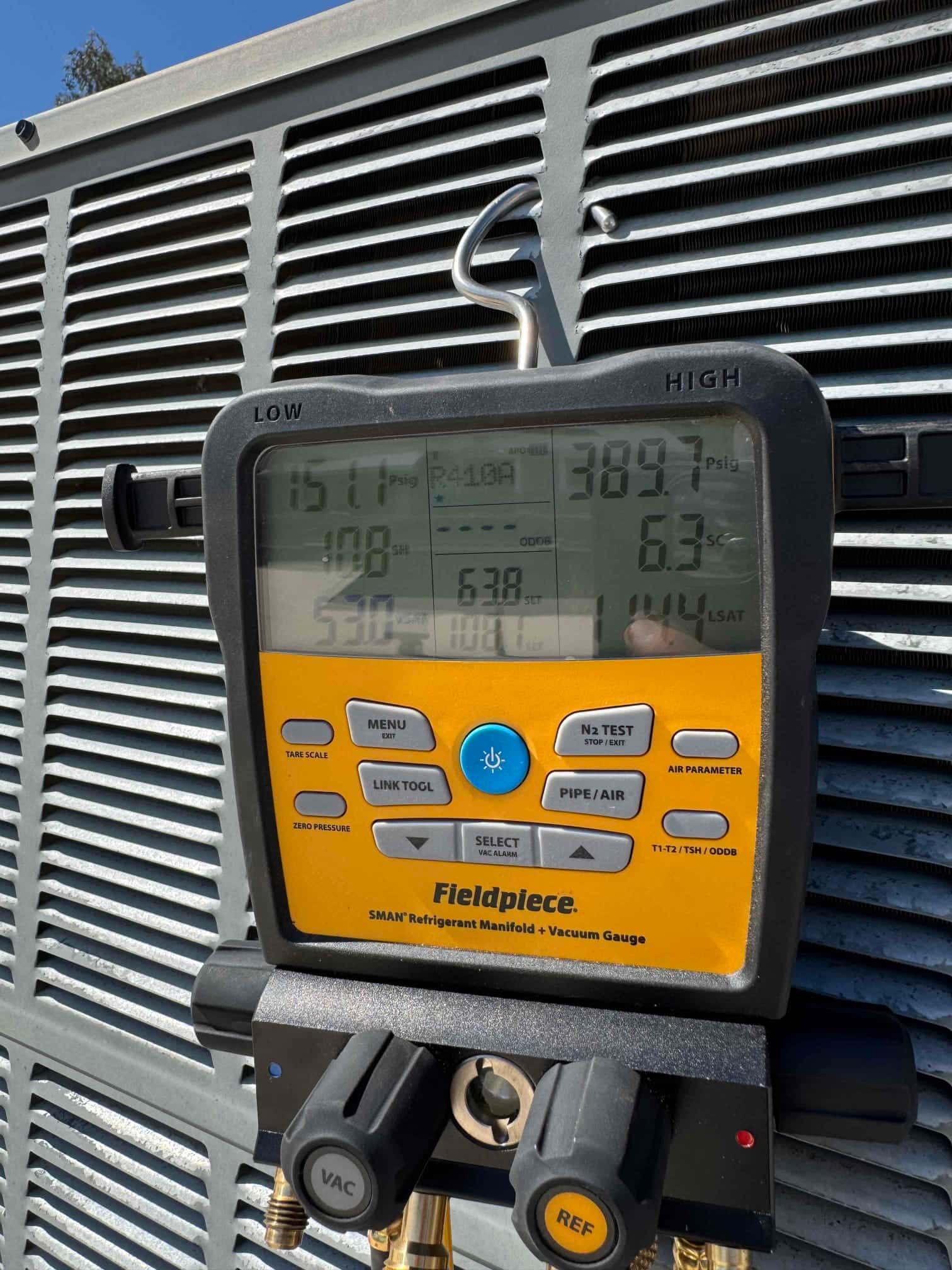Digital manifold gauge connected to an outdoor condenser shows high-side pressure of 389.7 psi on the HIGH port.