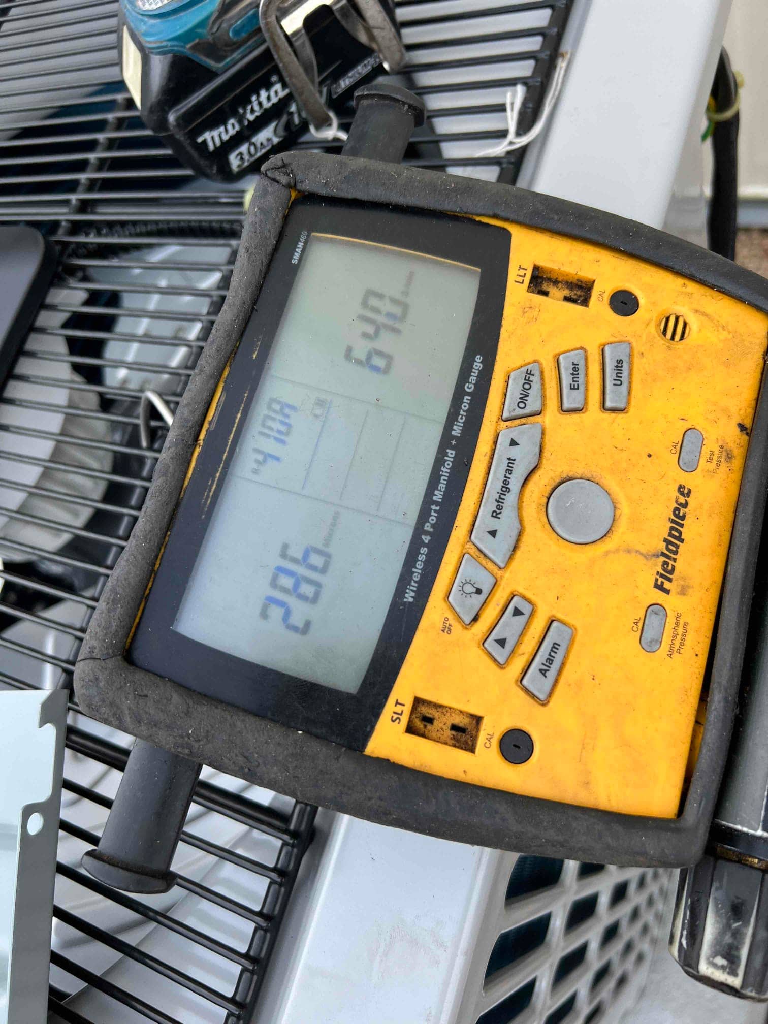 Digital manifold on the outdoor unit displays operating refrigerant pressures with distinct high and low side readings during commissioning.