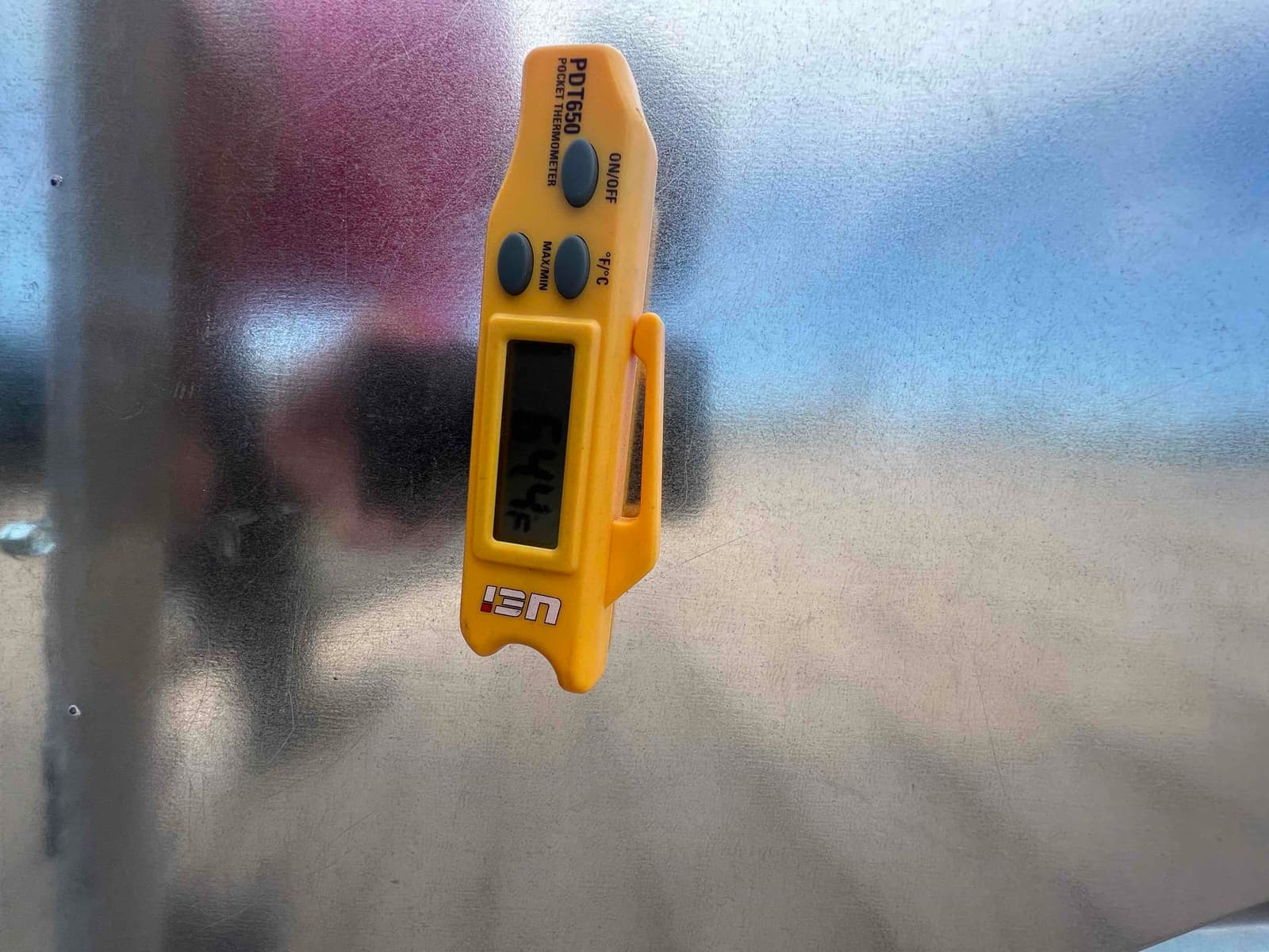 Digital pocket thermometer shows 64.4°F while checking air temperature on a metal HVAC surface during commissioning.