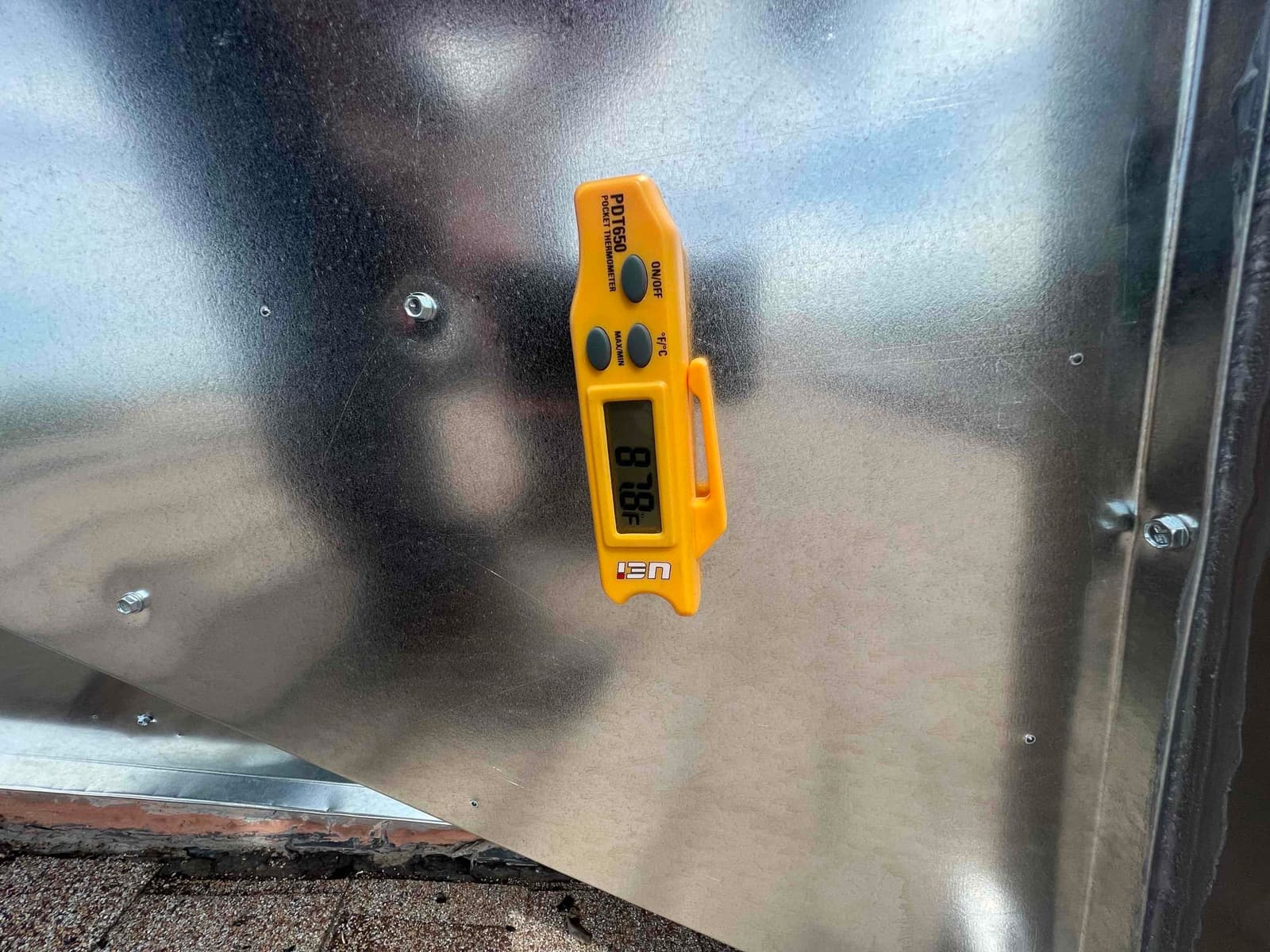 Digital thermometer attached to metal duct surface shows 70.8 degrees Fahrenheit during air-side temperature check.