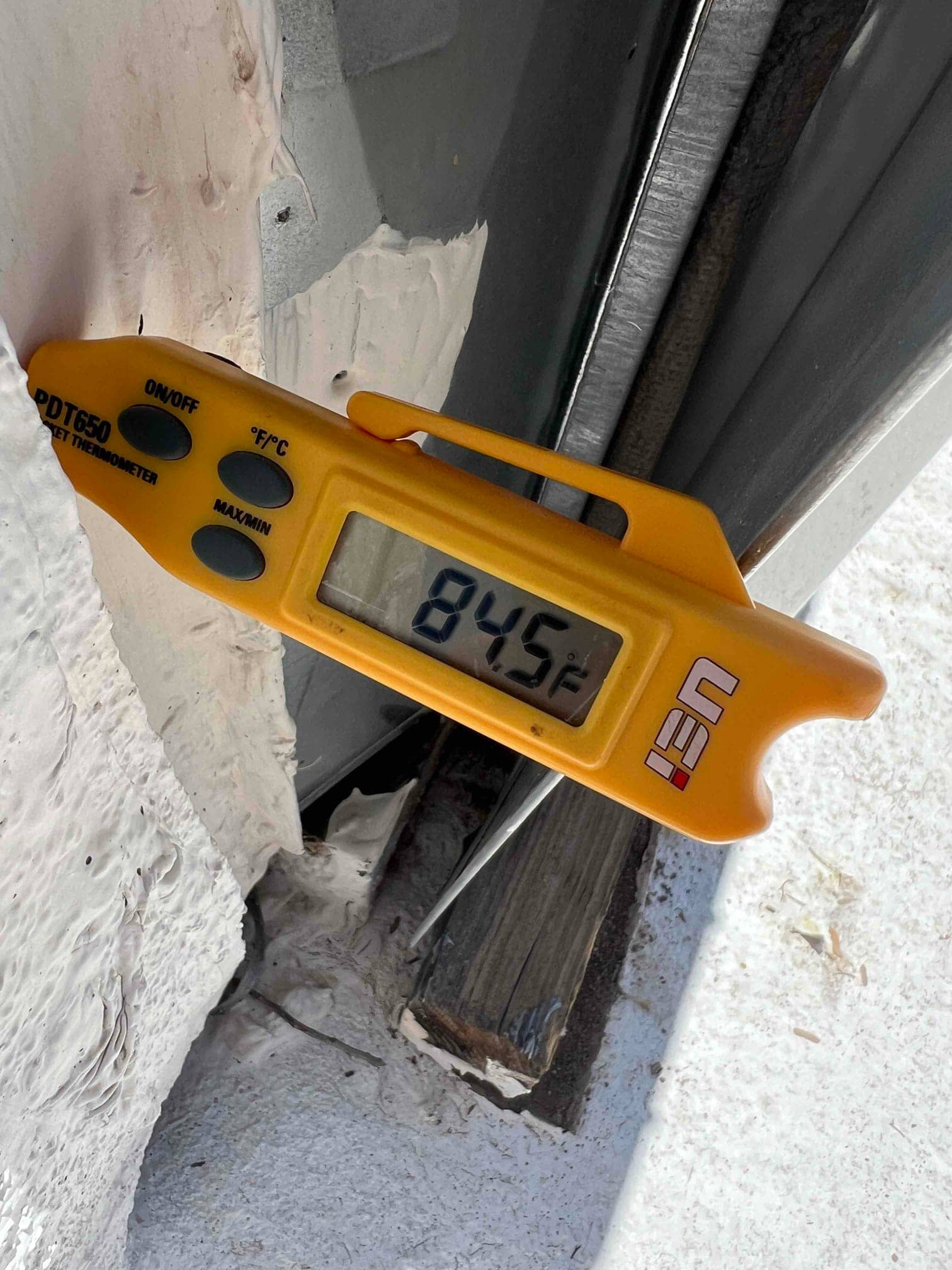 Digital thermometer displays 84.5°F while checking air temperature during HVAC commissioning.