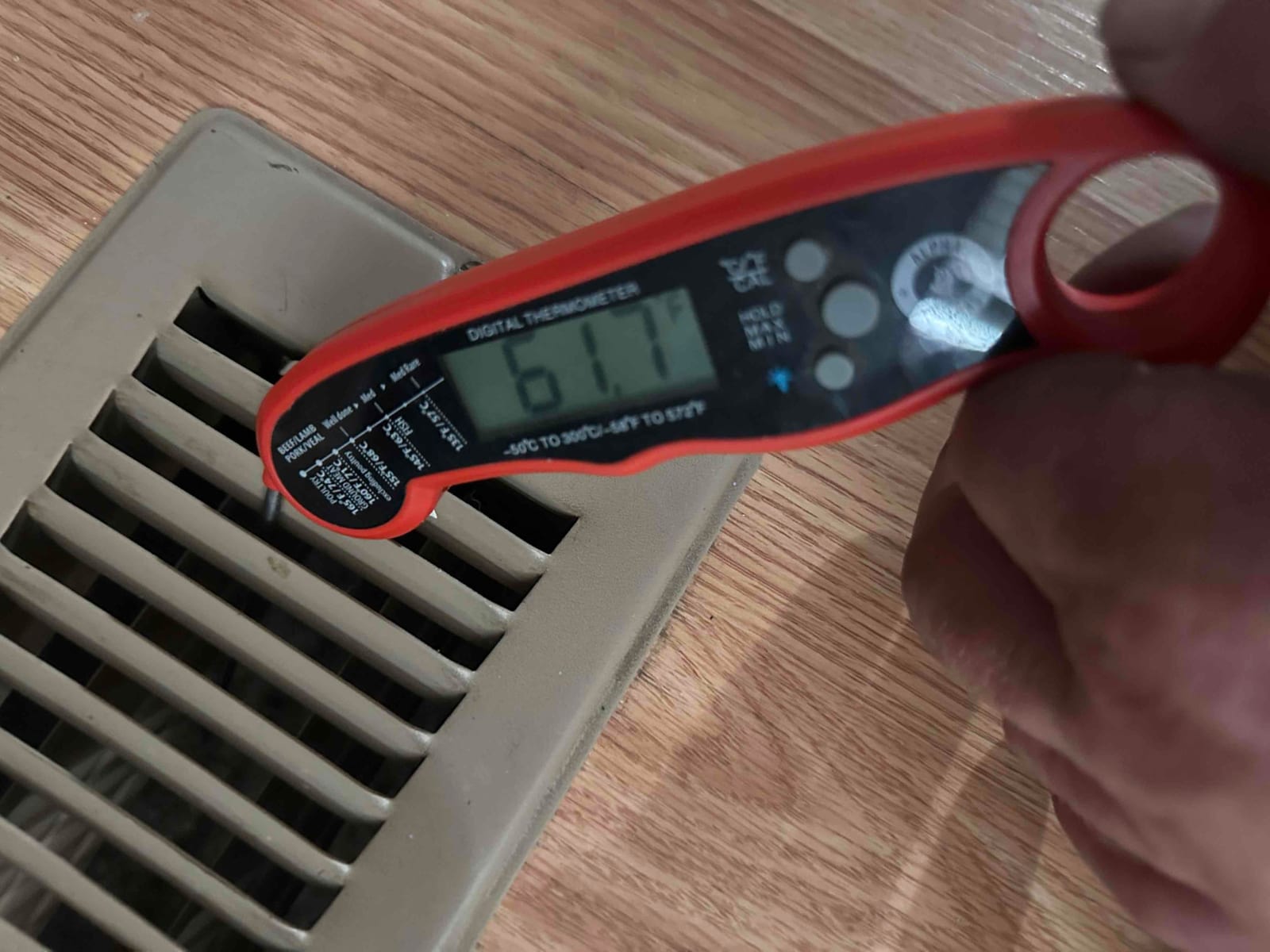 Digital thermometer at a floor supply register reads 61°F, documenting supply air temperature during system startup cooling check.
