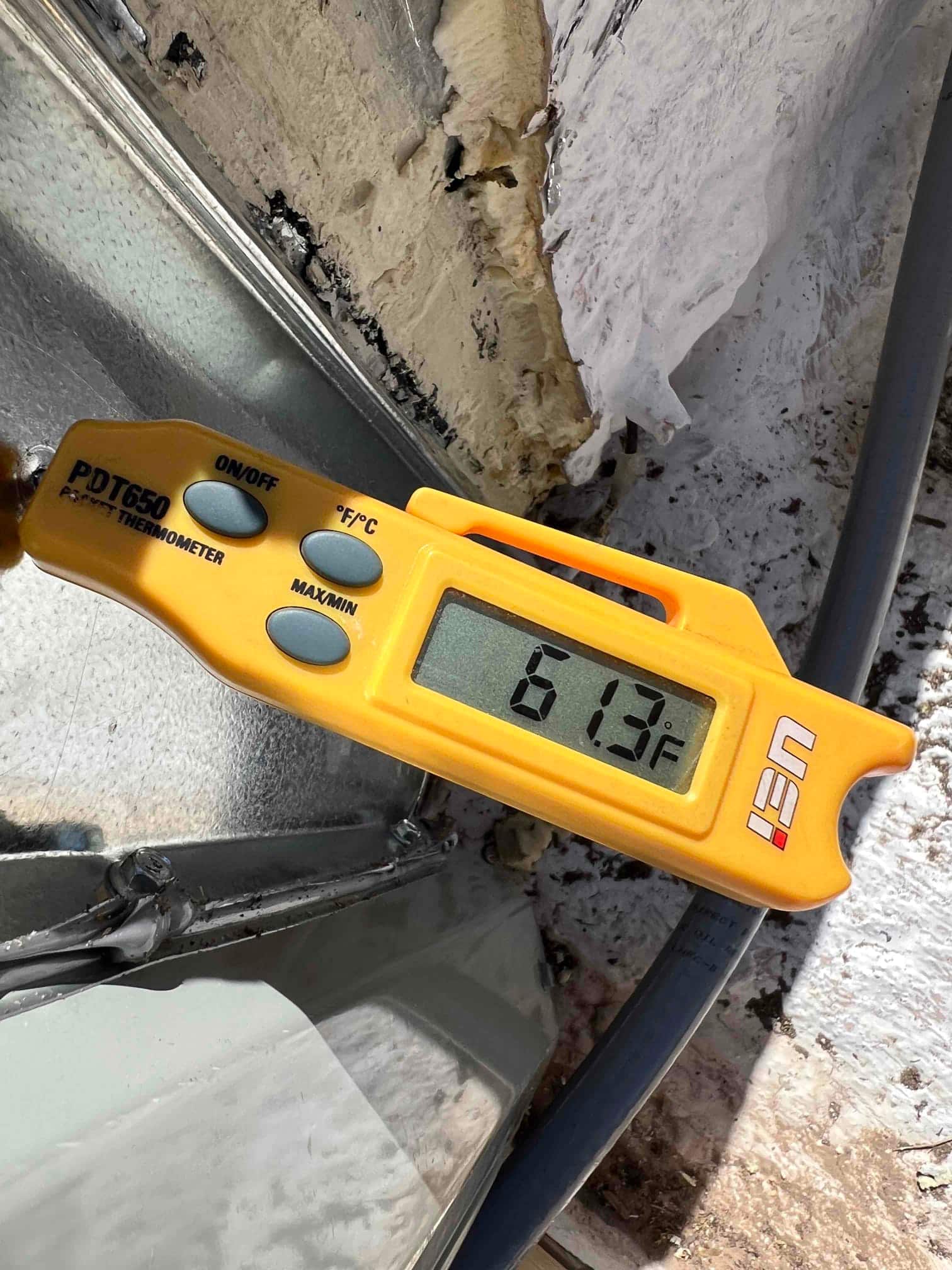 Digital thermometer probe measures 61.3°F at a duct surface during cooling air-side commissioning.
