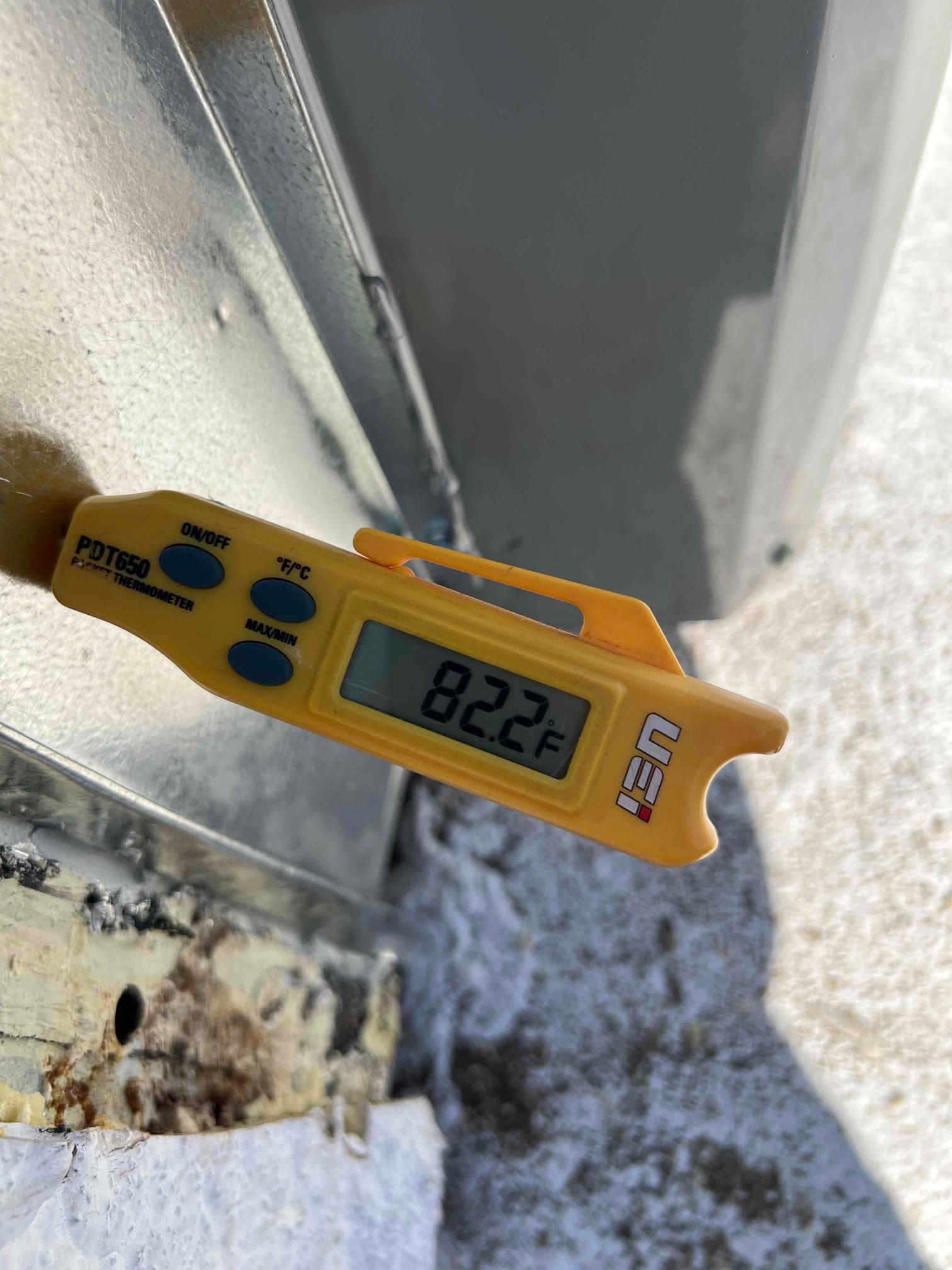 Digital thermometer probe measures return air temperature at 82.2°F during HVAC system commissioning.