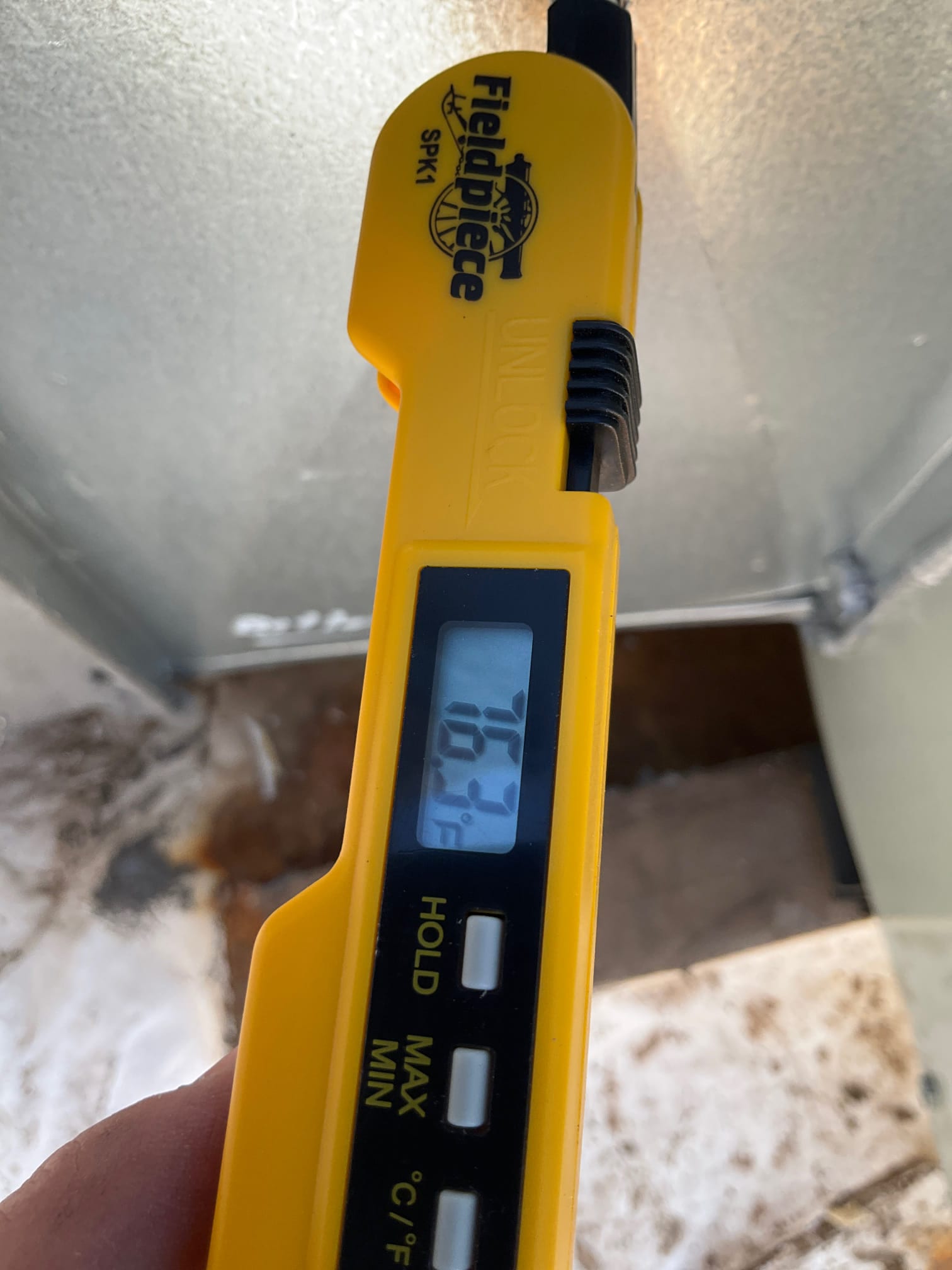 Digital thermometer probe shows 76.3°F air temperature reading during return-side airflow check at the duct opening.