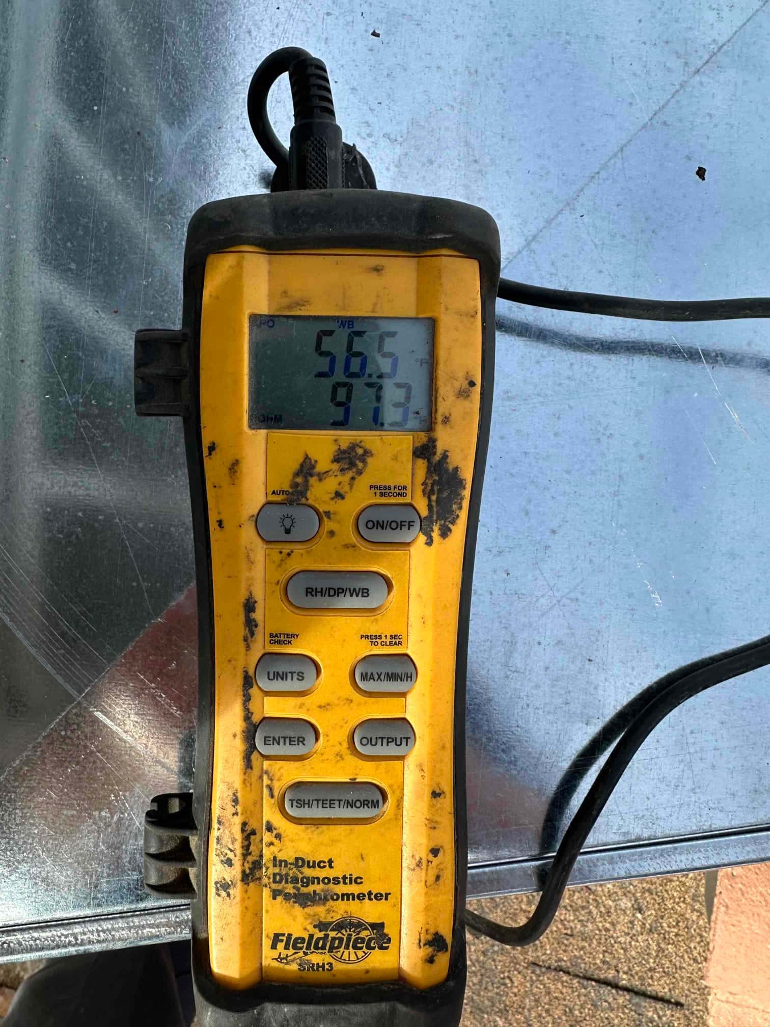 Digital thermometer rests on ductwork showing 56.5°F and 97.3 on the display during air-side commissioning.