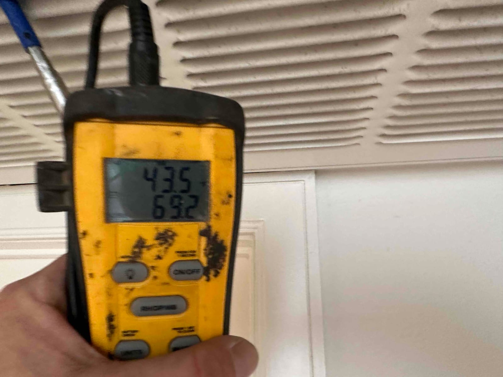 Digital thermometer at a return grille displays 69.2°F with probe inserted, documenting return air temperature during commissioning.