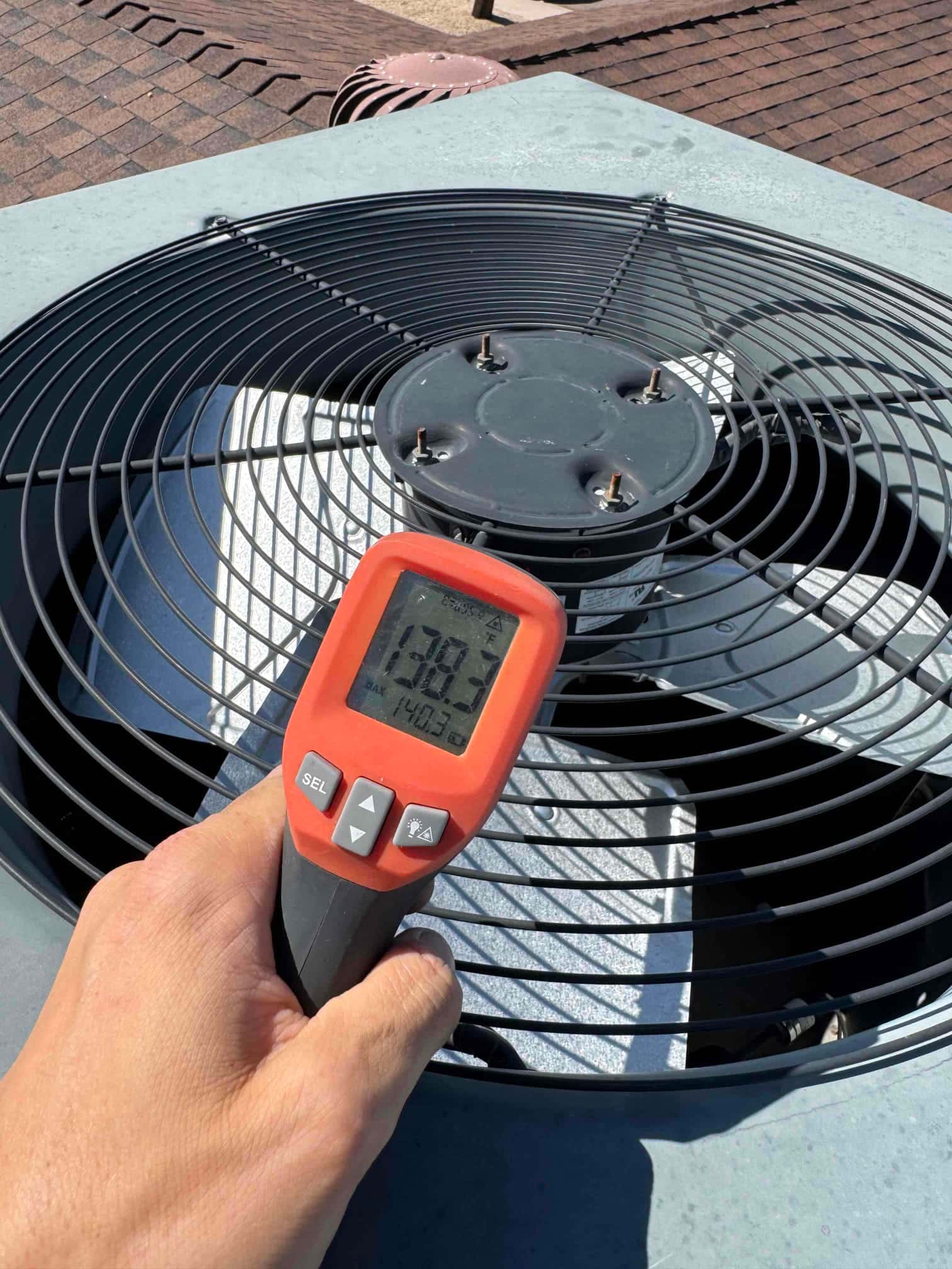 Digital thermometer shows 138.2 °F while measuring the air temperature above the running outdoor condenser fan.