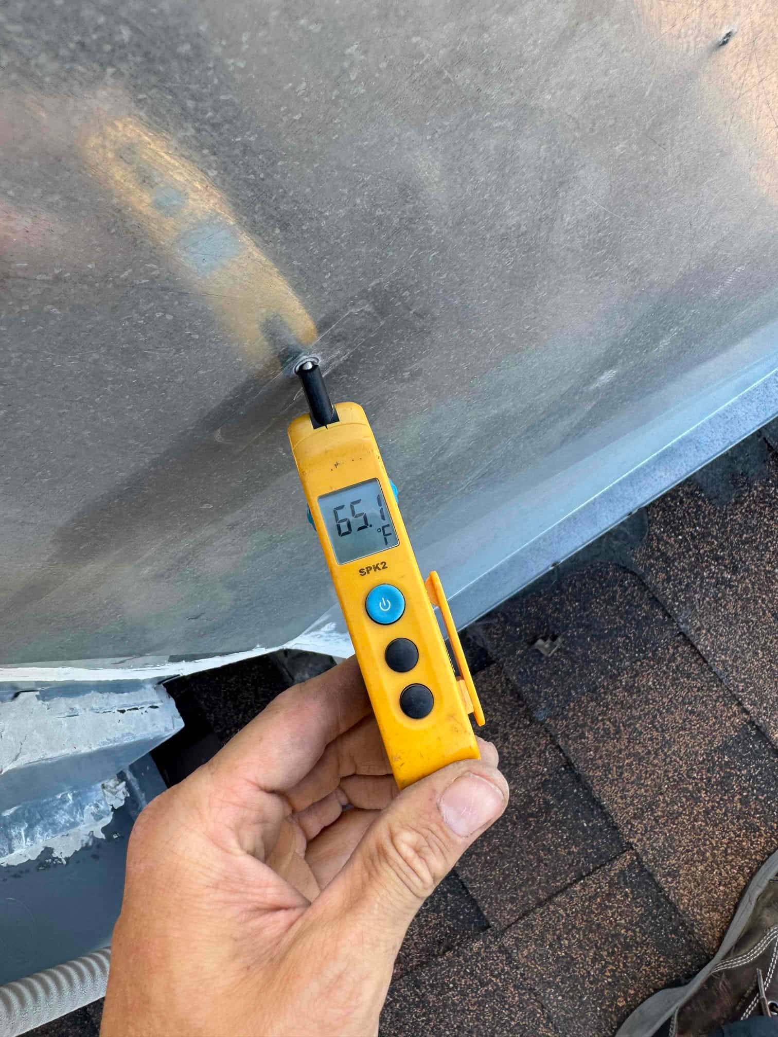 Digital thermometer shows 65.7 °F surface temperature on the outdoor HVAC unit housing during air conditioning repair.