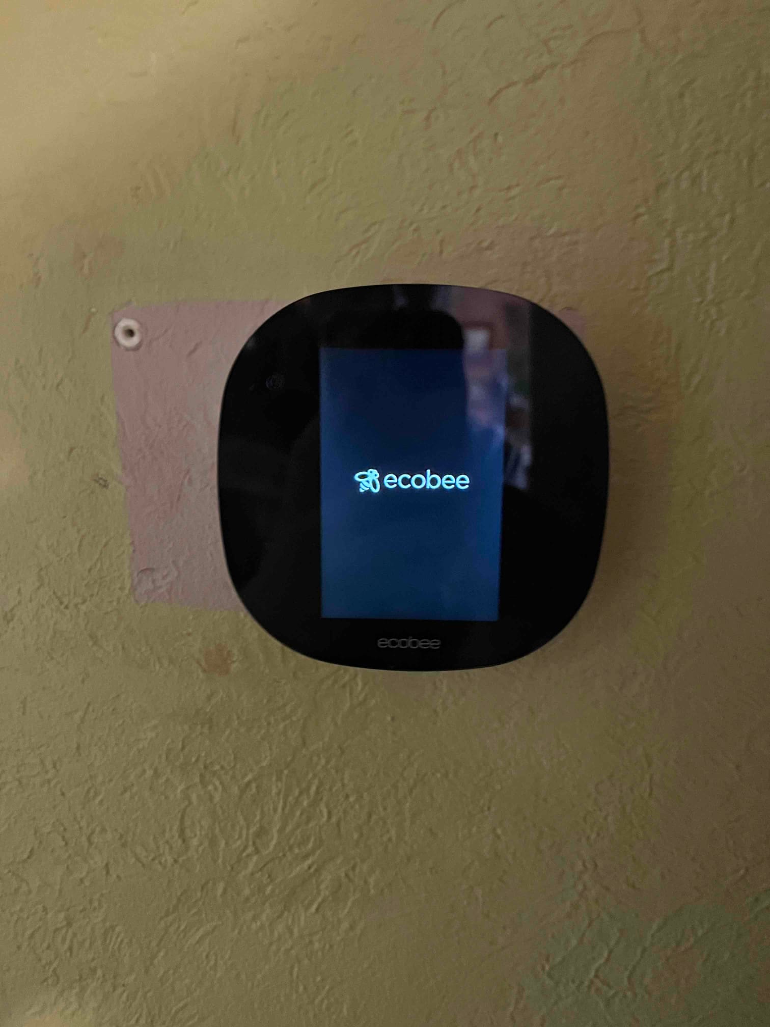 Ecobee smart thermostat mounted on the wall, powering on and displaying the startup logo on its screen.