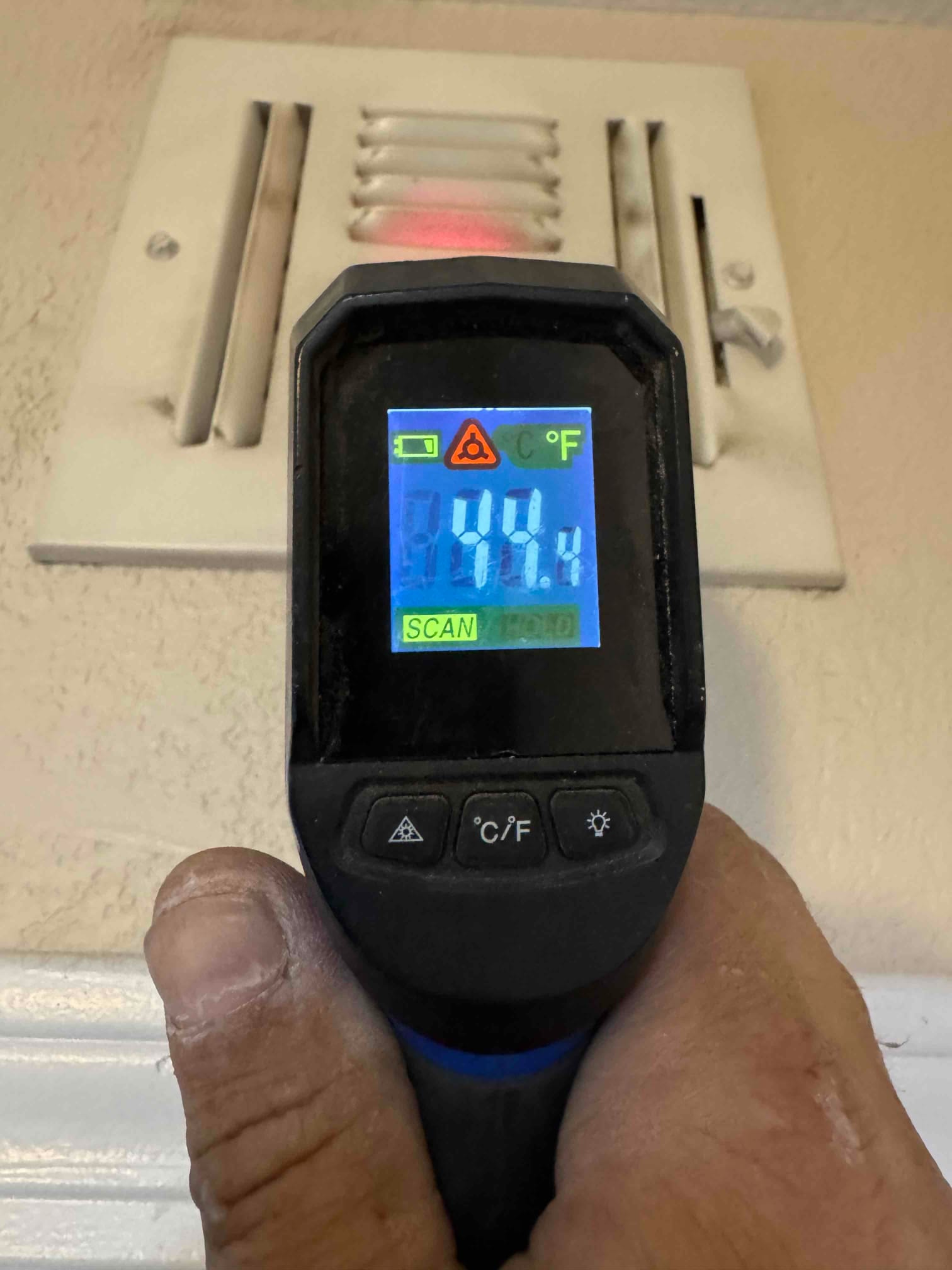 Infrared thermometer aimed at a supply register shows 44.4 degrees Fahrenheit during cooling verification.