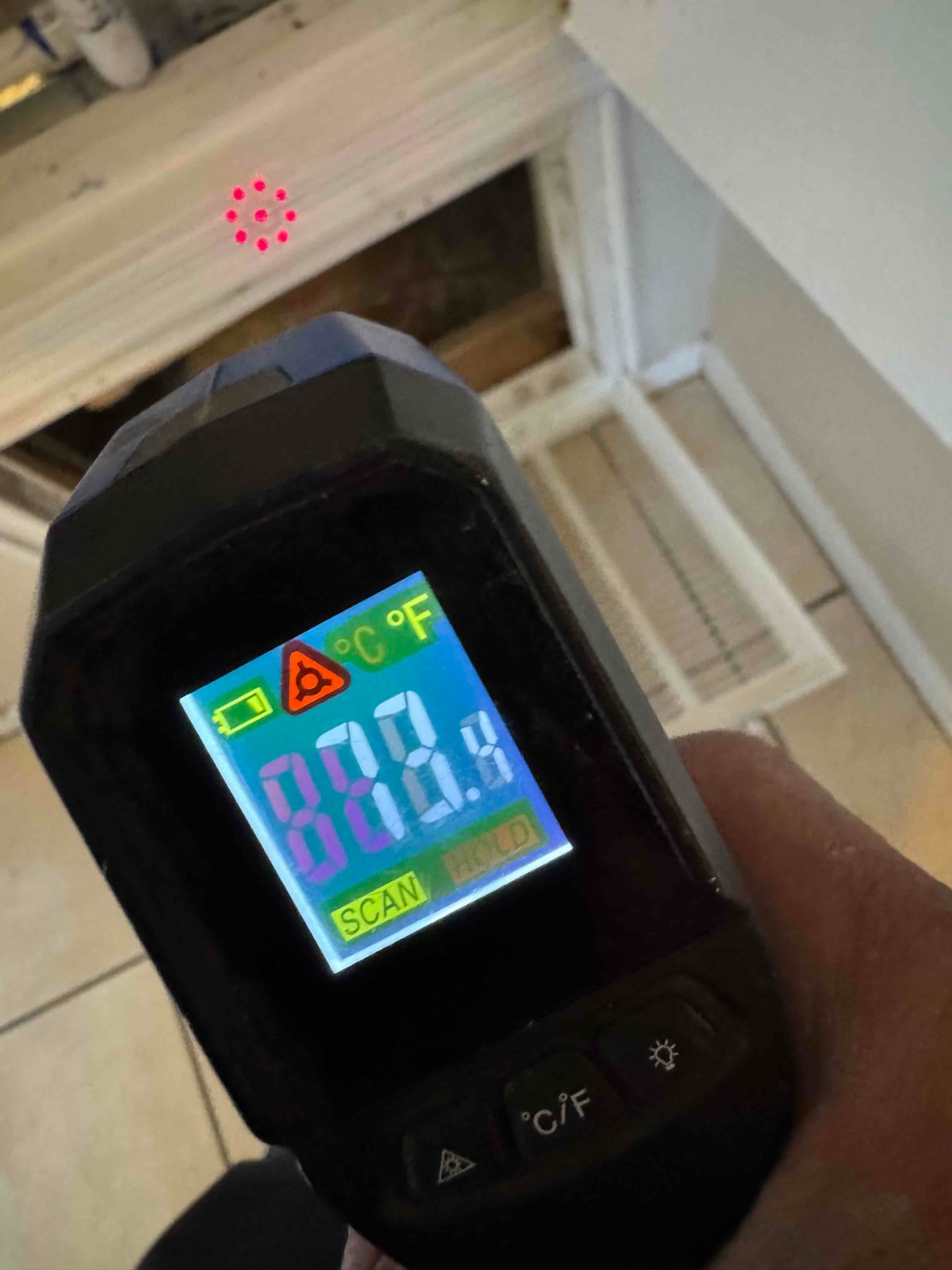Infrared thermometer scans a supply register during commissioning to verify discharge air temperature at the vent.
