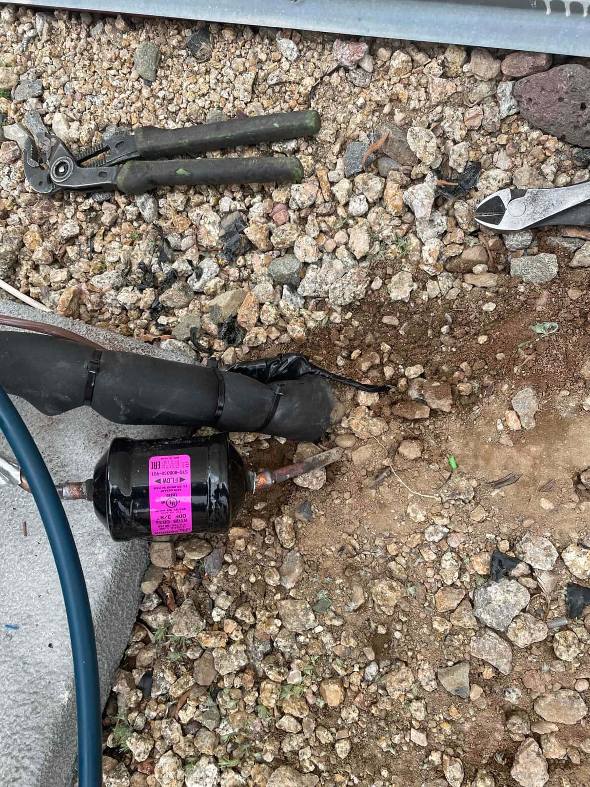 Liquid-line filter drier with copper stubs and insulated refrigerant line set on the ground during installation, with hand tools nearby.