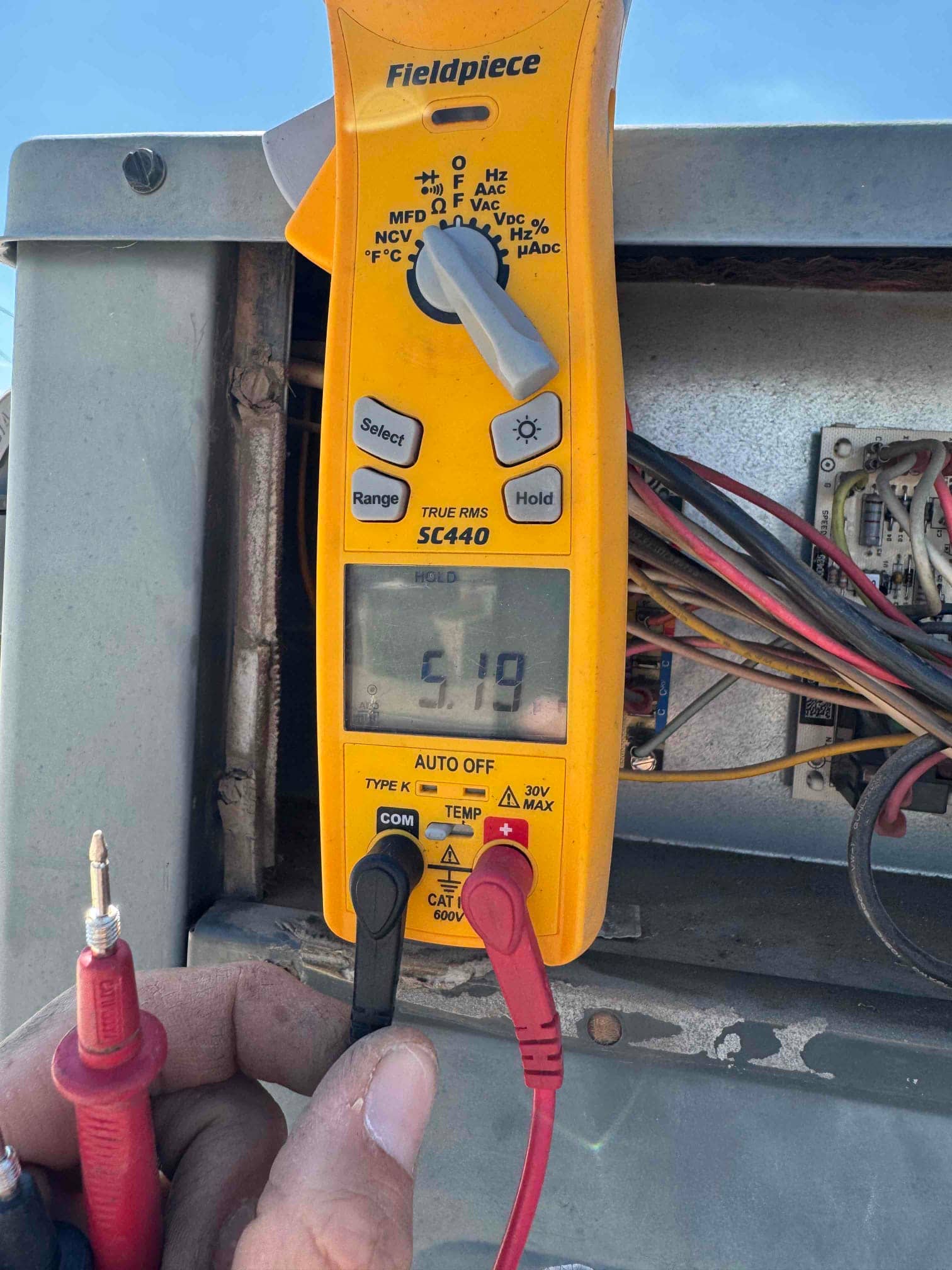 Multimeter measures 5.19 V at the control board terminals inside the outdoor condenser cabinet during diagnostic testing.