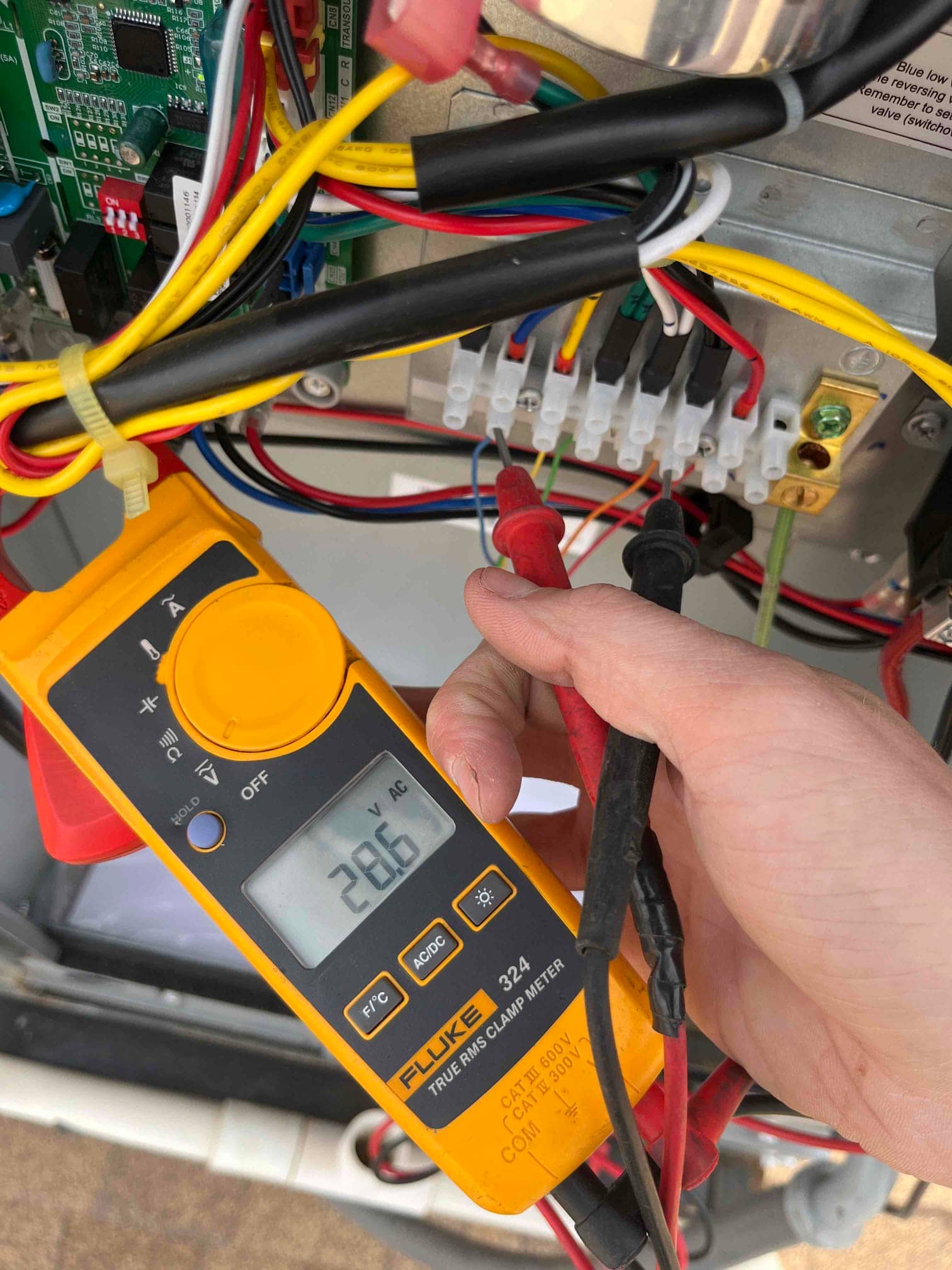 Multimeter probes a control terminal block, displaying 28.65 V on the meter screen during testing.