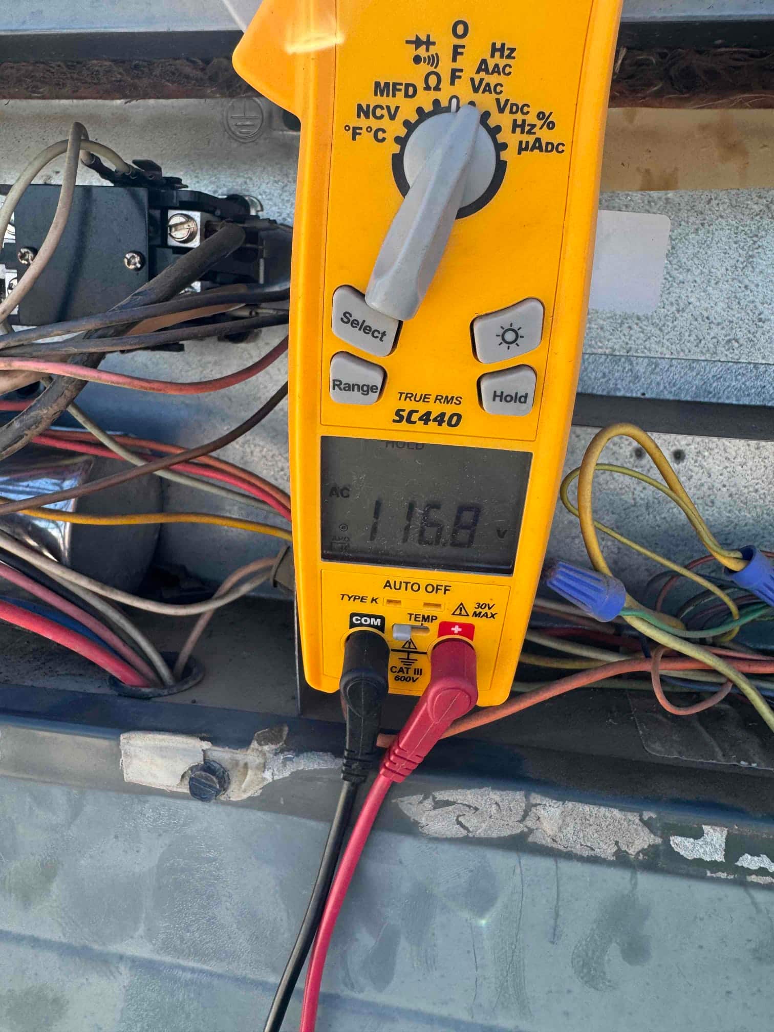 Multimeter set to AC voltage shows 116.8 V across two control circuit terminals at the outdoor unit.