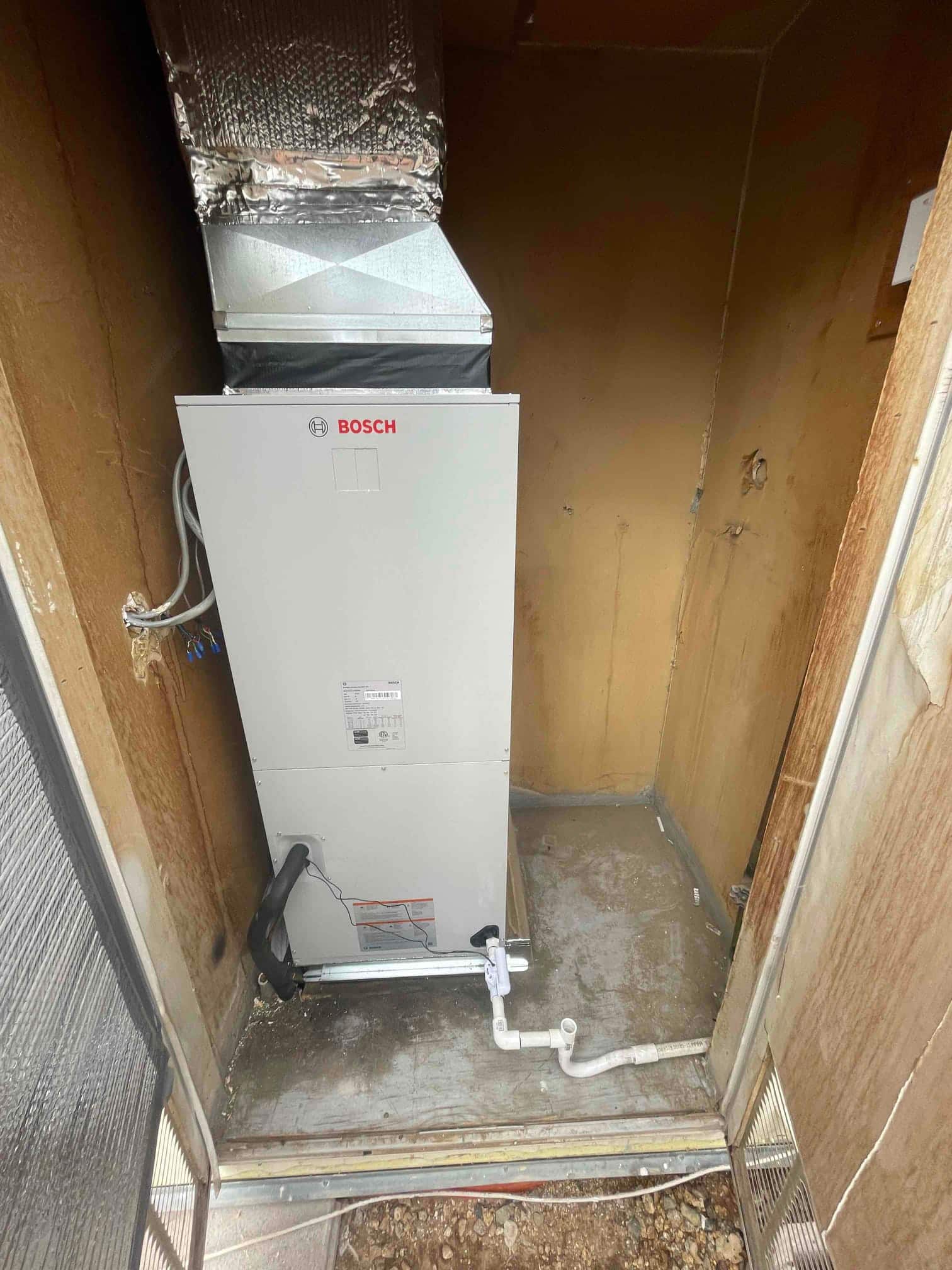 New air handler installed in closet with connected duct transition, insulated refrigerant line, and condensate drain piping.