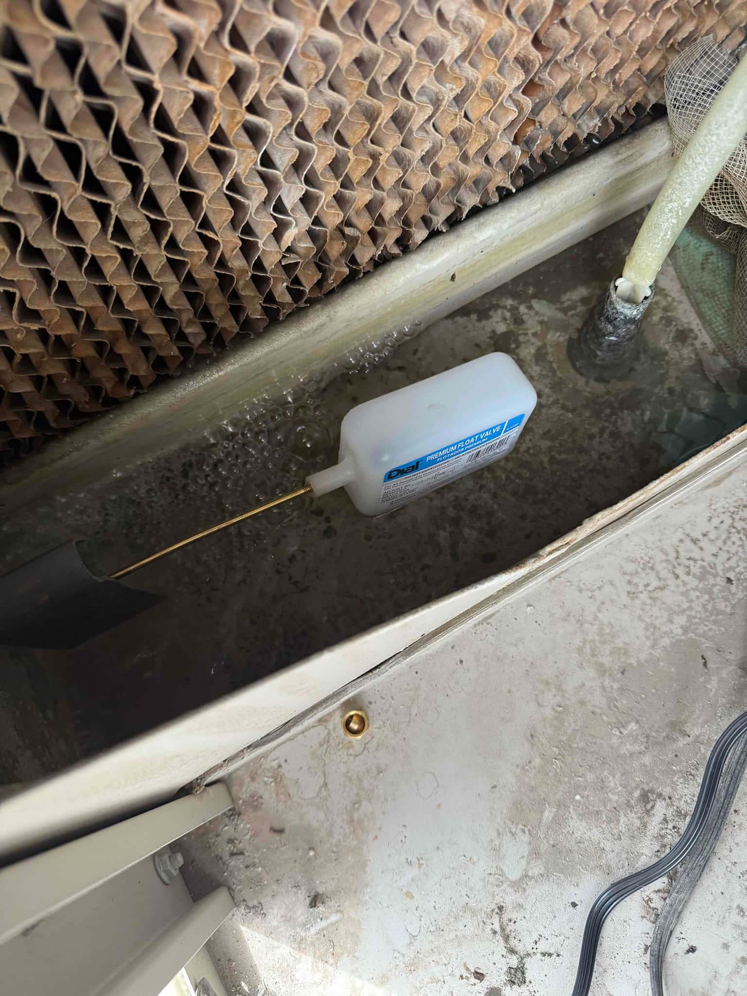 New float valve installed inside the evaporative cooler reservoir, with water level rising and pad media visible above.