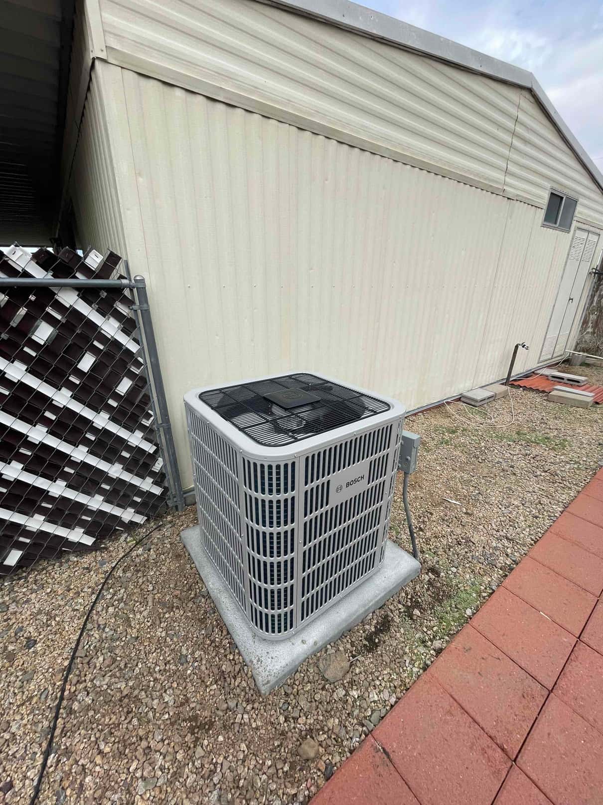 New outdoor condenser set on a level pad with connected disconnect box and insulated refrigerant line at the installation site.
