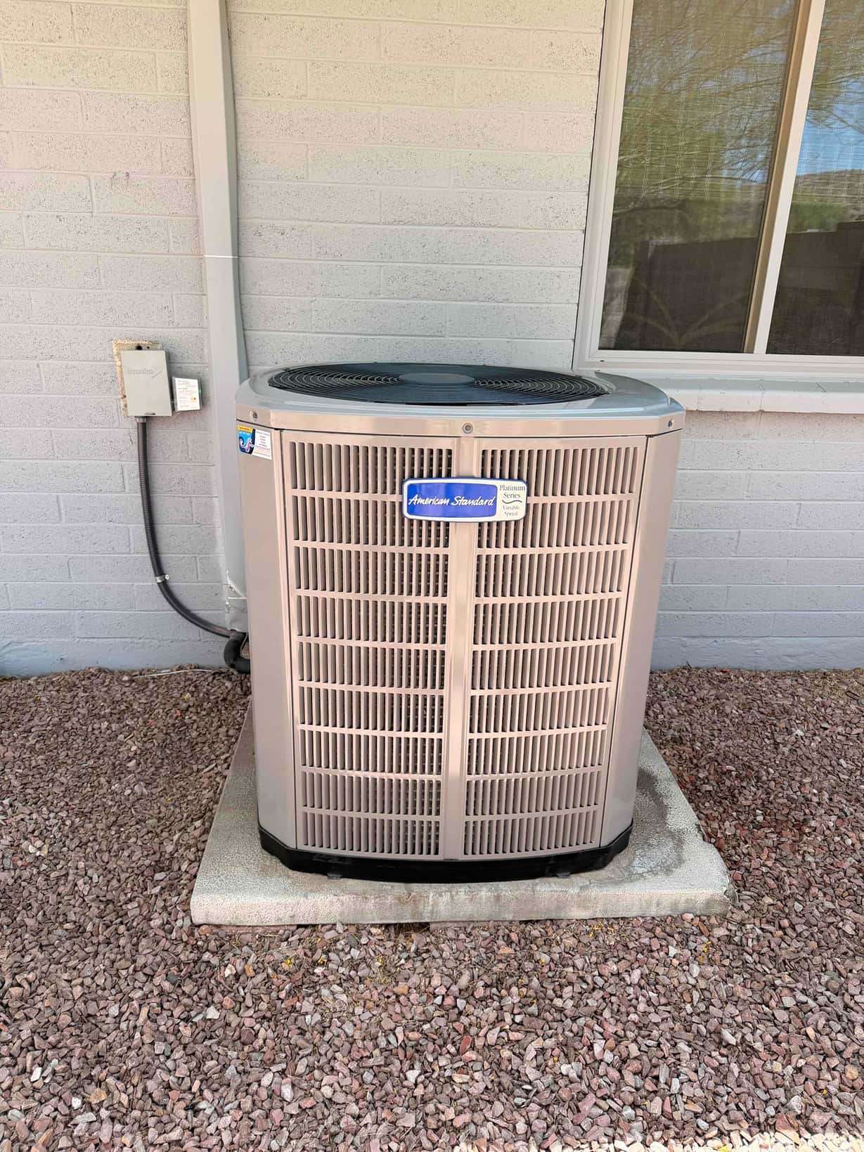 New outdoor condenser set on a level pad with electrical disconnect and line set cover installed beside the exterior wall.