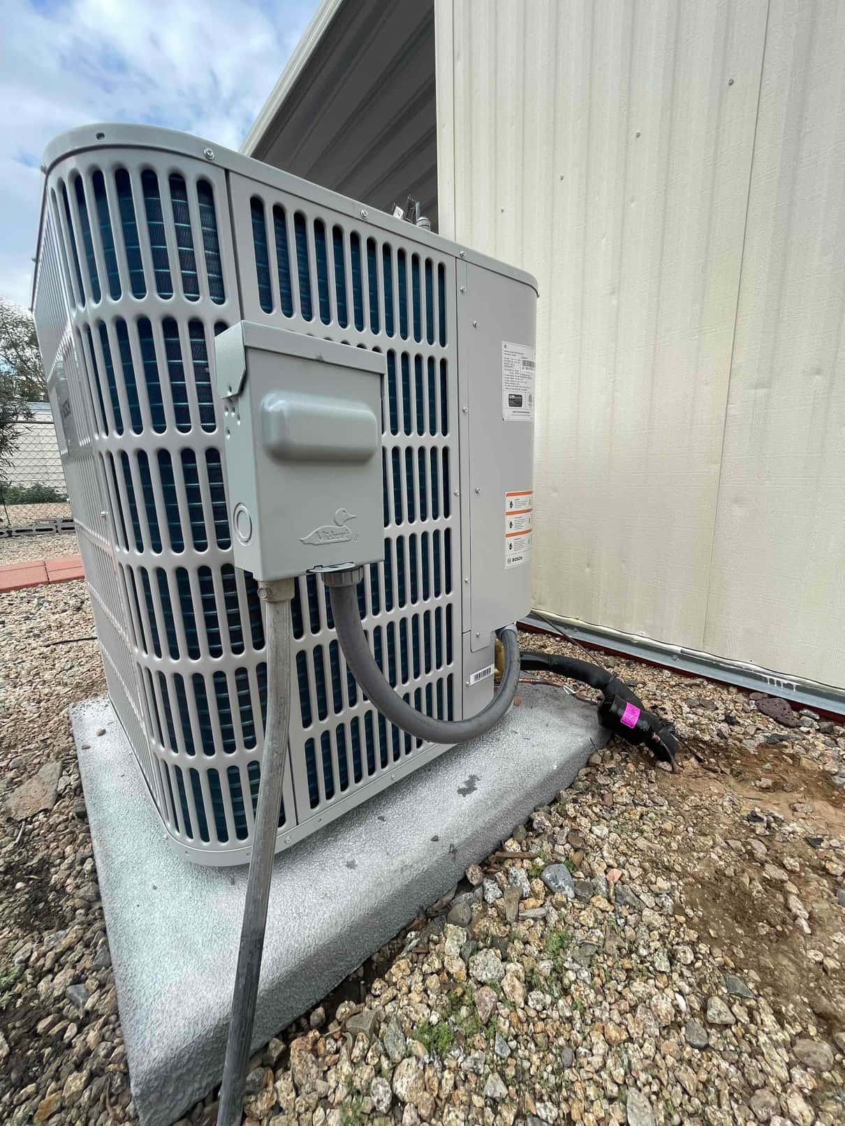 New outdoor condenser set on a level pad with electrical whip and insulated refrigerant lines routed to the wall penetration.